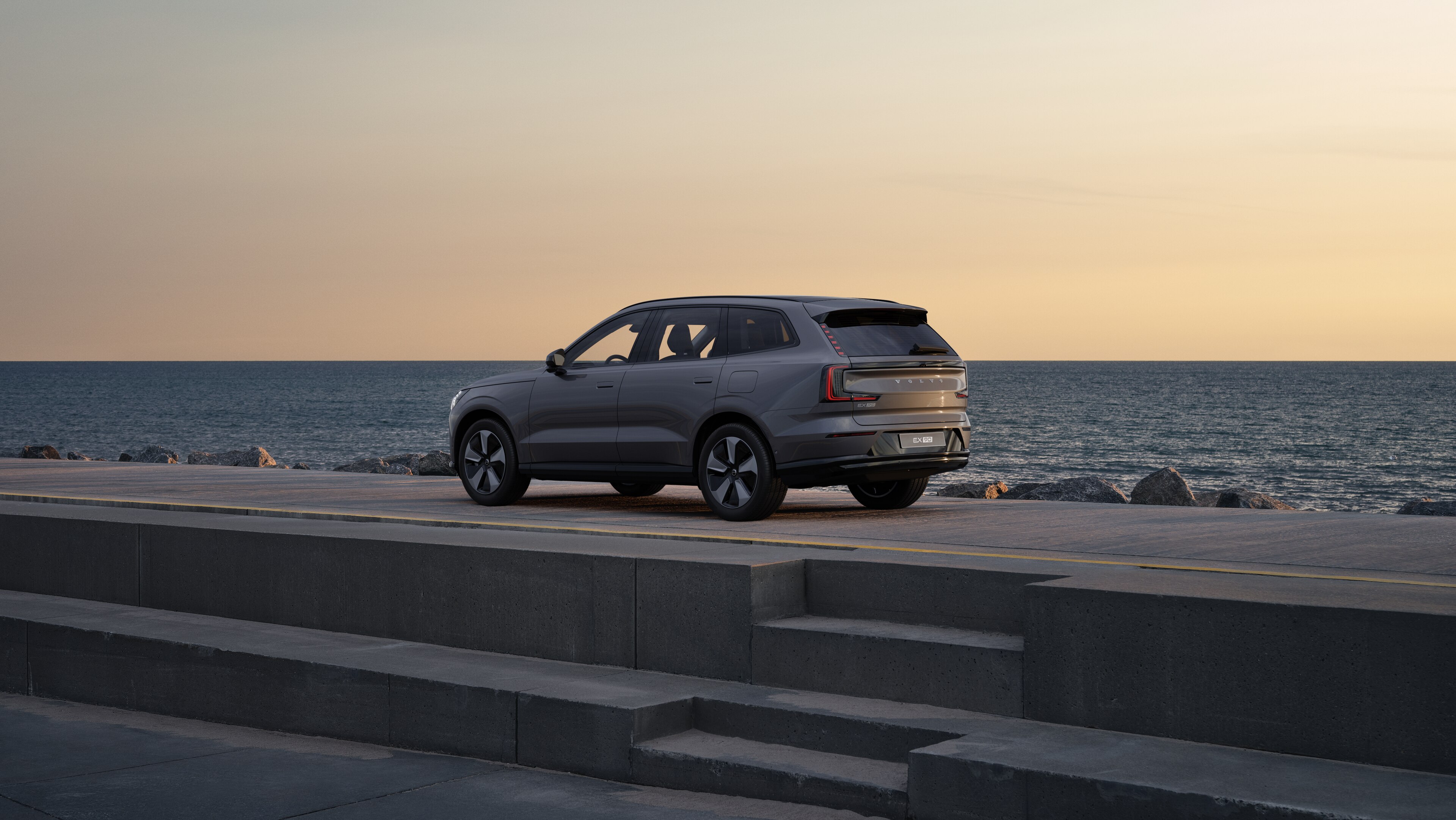 Volvo en vue arrière de trois quarts, garée contre un mur en béton dans une rue urbaine.