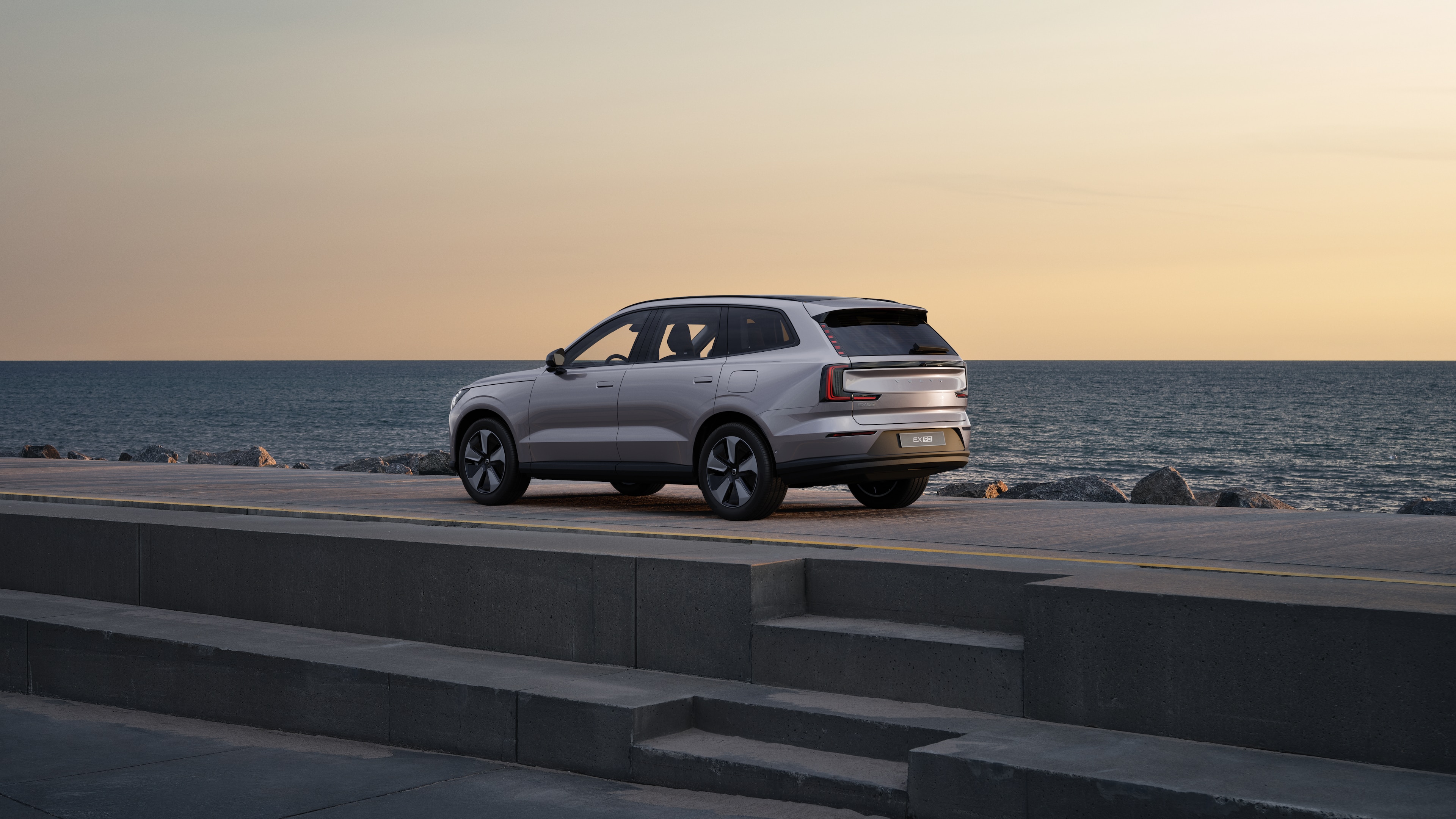 Voiture Volvo en vue arrière de trois quarts, garée contre un mur en béton sur un fond de rue urbaine.