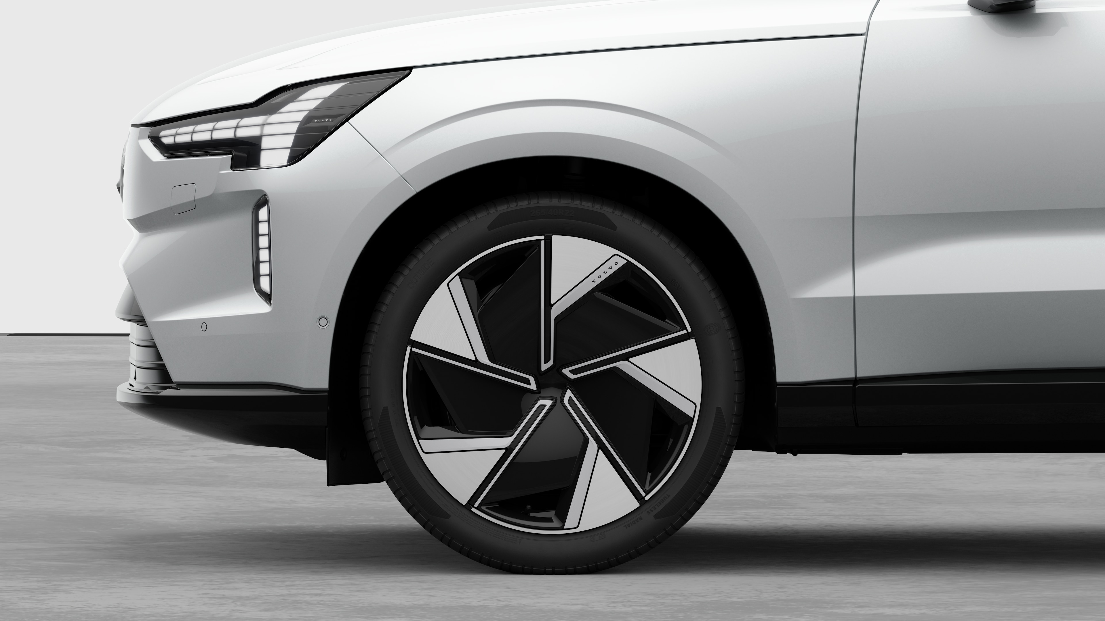 Zijaanzicht van de buitenkant van een Volvo auto, gericht op het voorwiel en het spatbord, tegen een effen studioachtergrond.