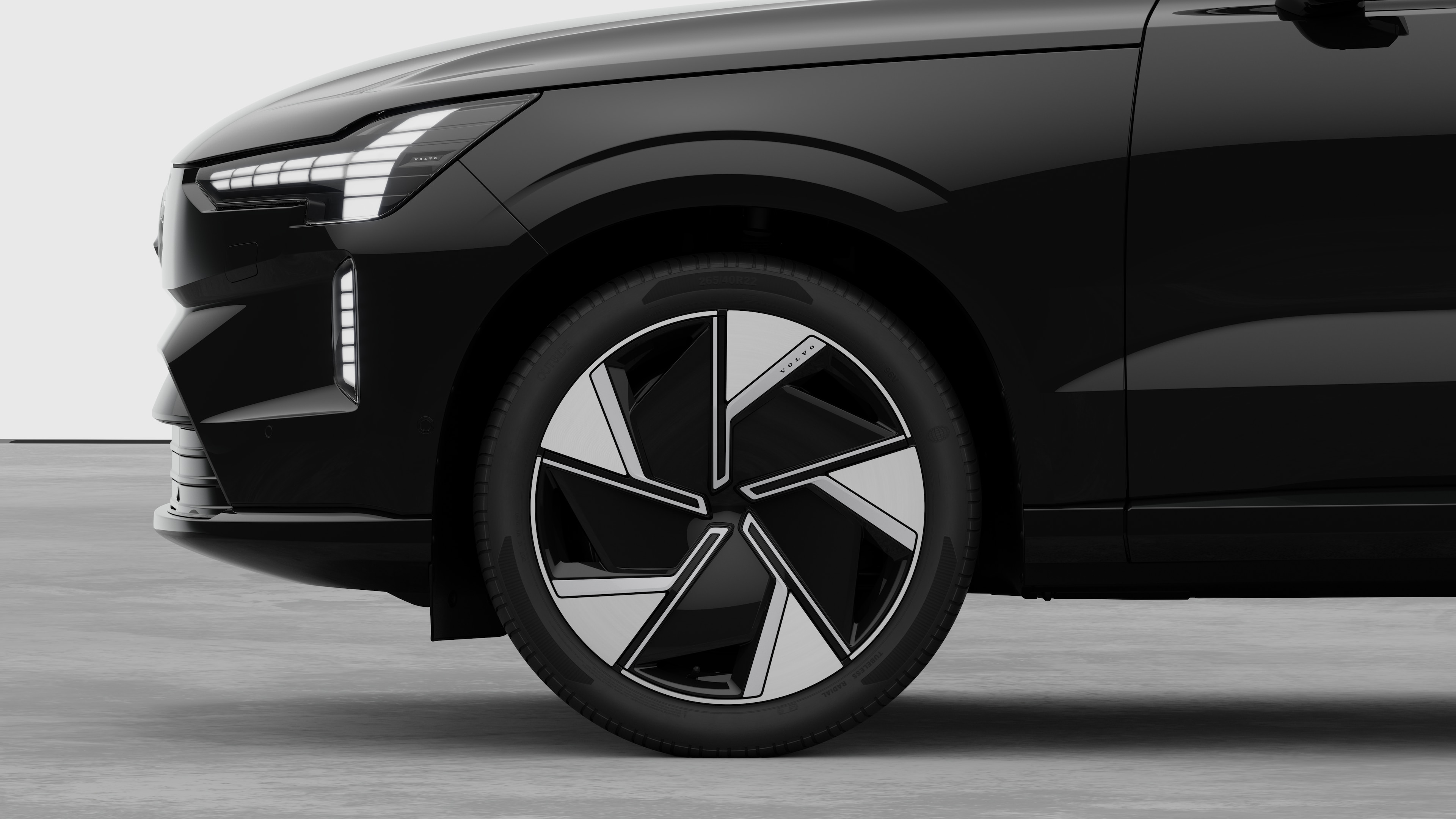 Zijaanzicht van de buitenkant van een Volvo auto, gericht op het voorwiel en het spatbord, tegen een effen studioachtergrond.