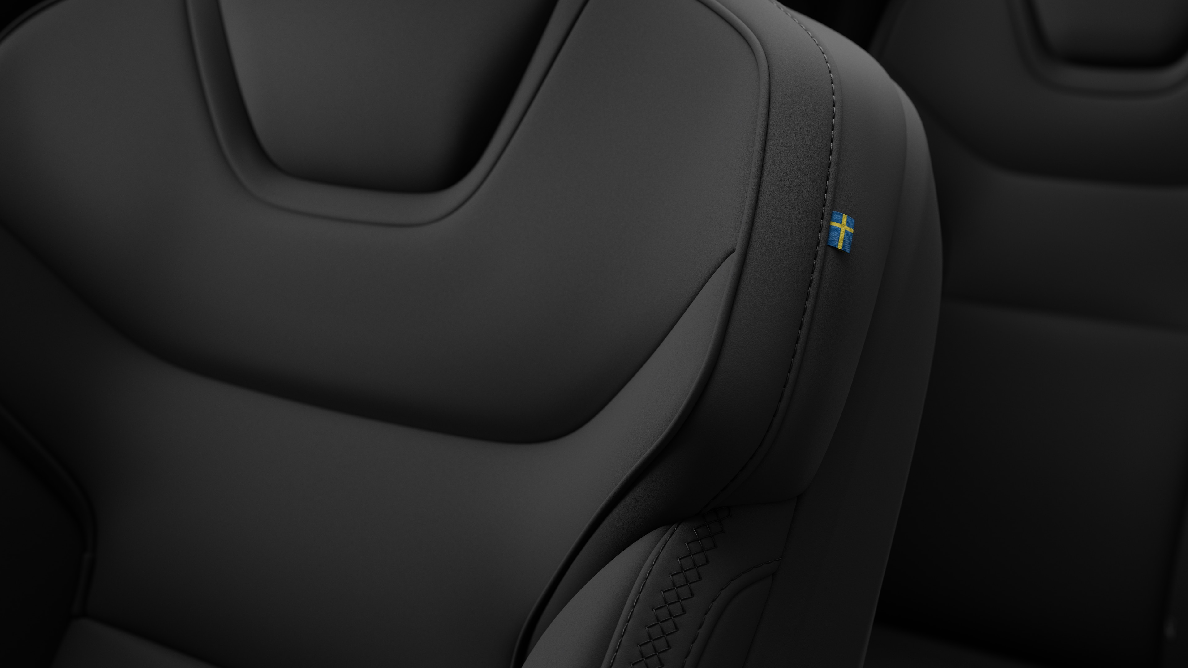 "Volvo" automobilio salono sėdynės detalė iš arti, kurioje pavaizduotos siūlės ir maža Švedijos vėliavos etiketė.