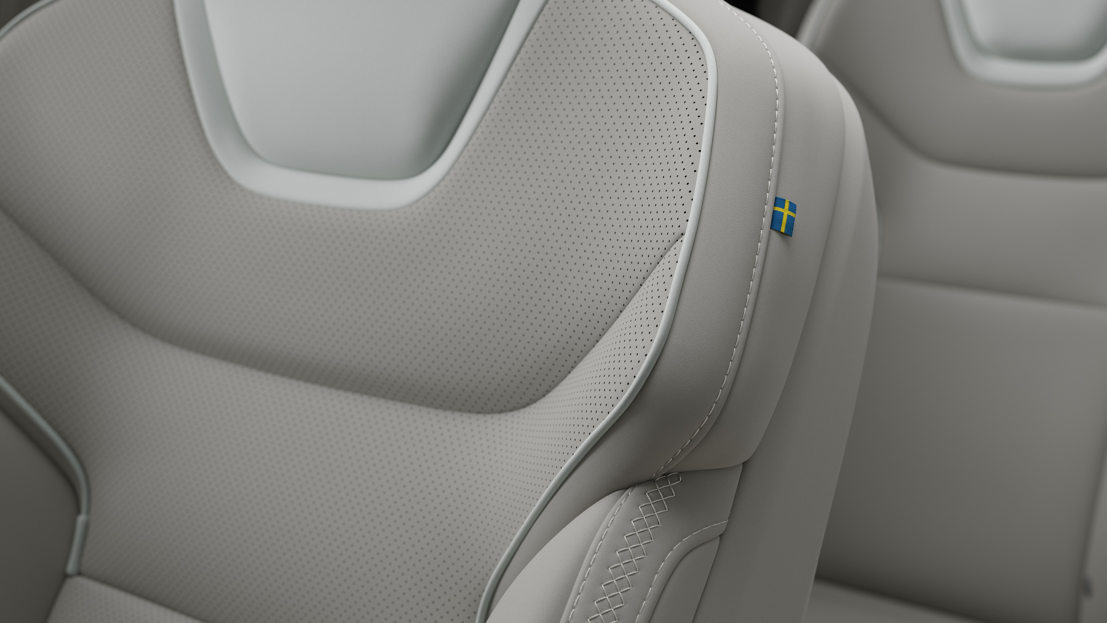 Närbild av Volvo Cars interiör, sätesdetalj som visar sömmar och en liten svensk flagga.
