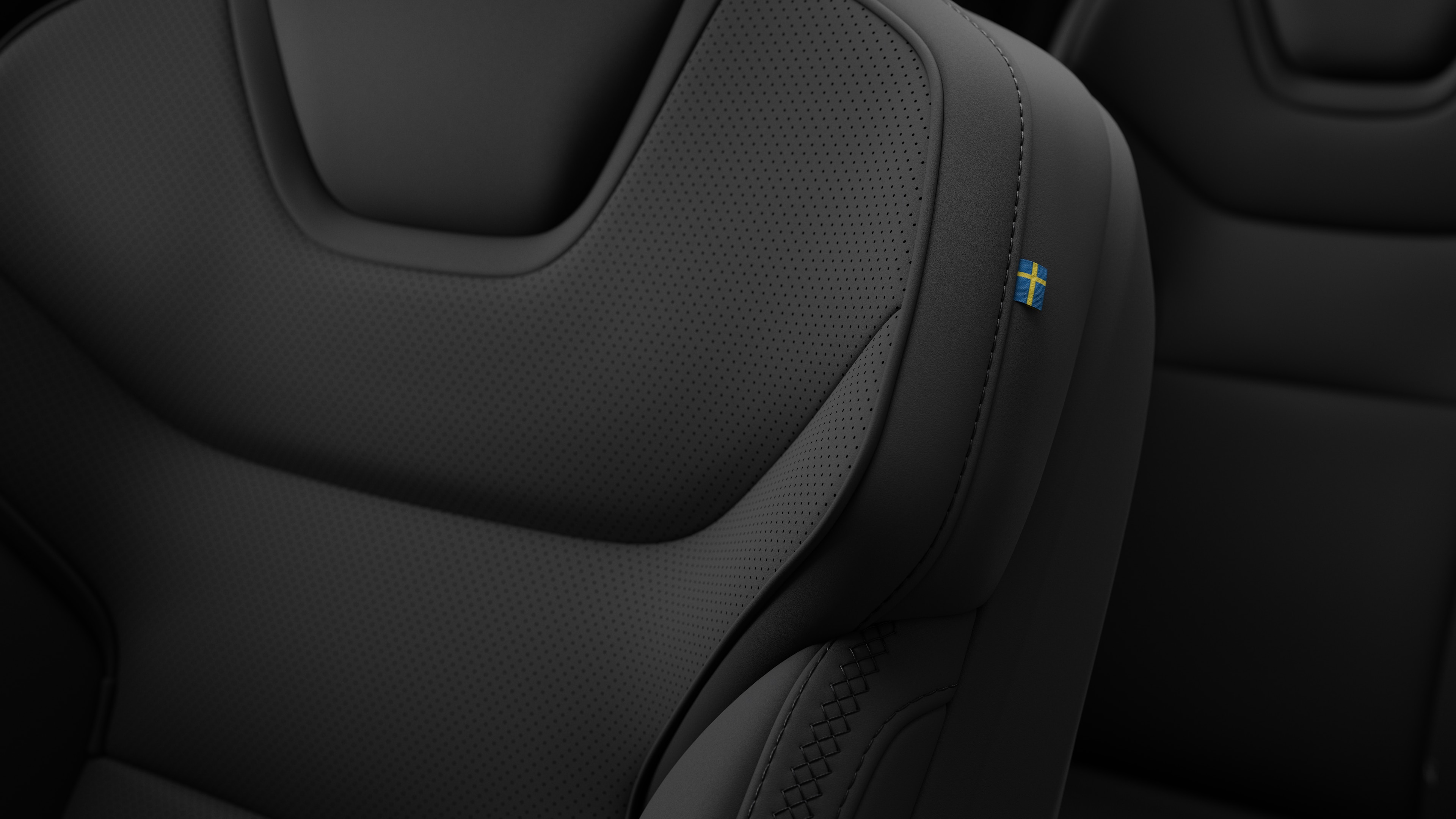 Zbliżenie na detale foteli we wnętrzu samochodu Volvo z widocznymi przeszyciami i małą plakietką z flagą szwedzką