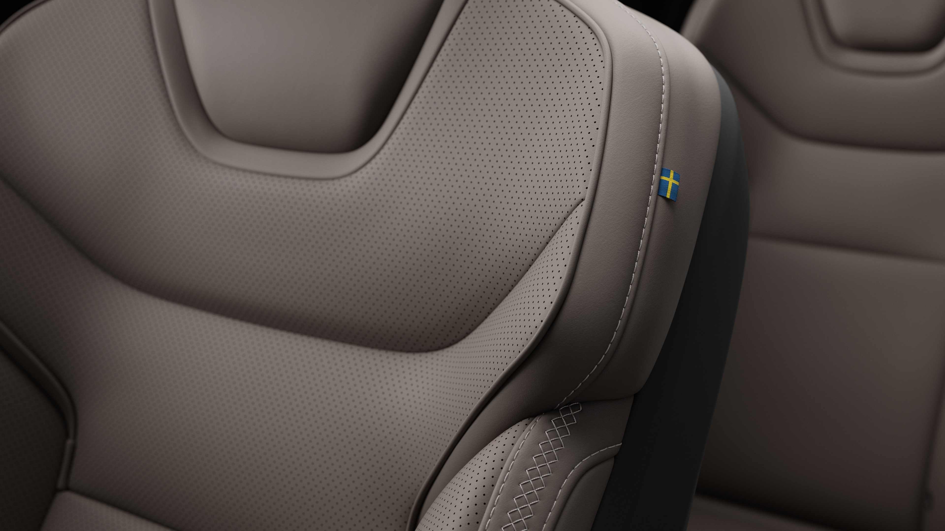 Närbild av Volvo Cars interiör, sätesdetalj som visar sömmar och en liten svensk flagga.