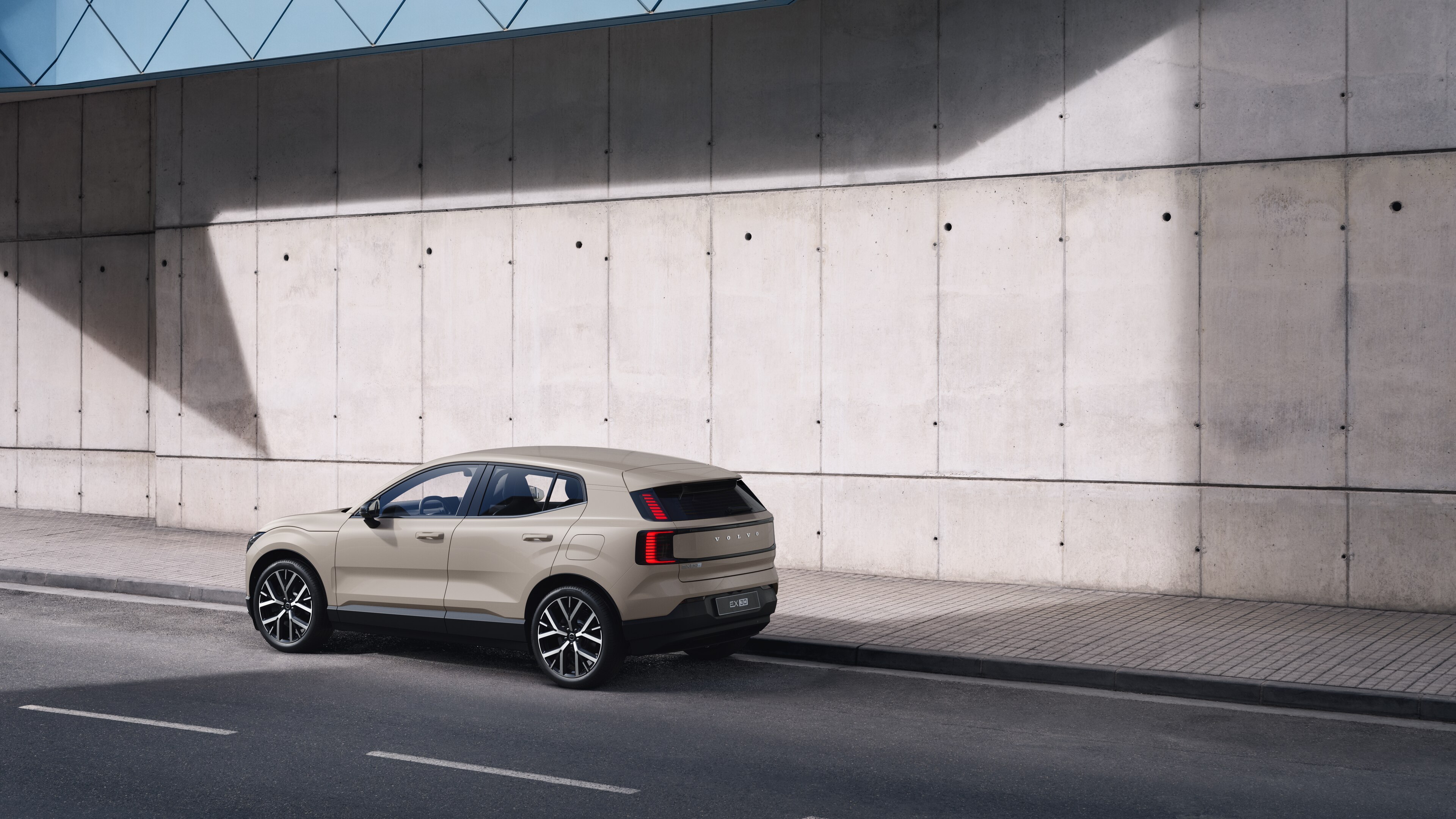 Volvo car in rear three-quarter view parked against a concrete wall on an urban street background.