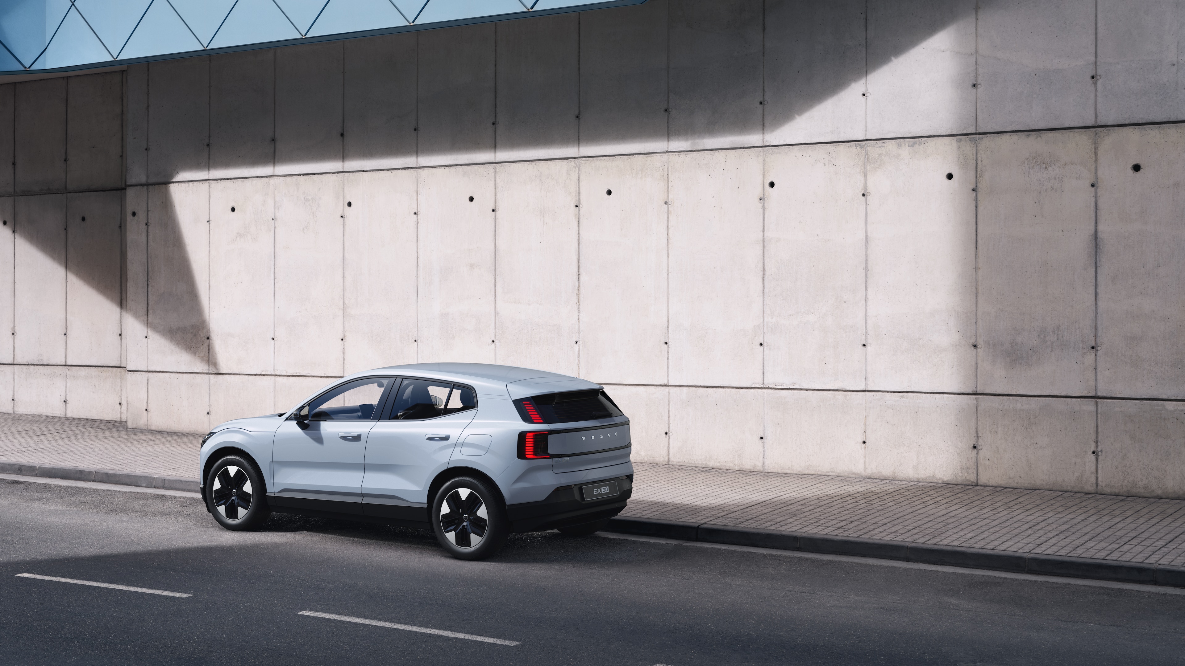 Volvo car in rear three-quarter view parked against a concrete wall on an urban street background.