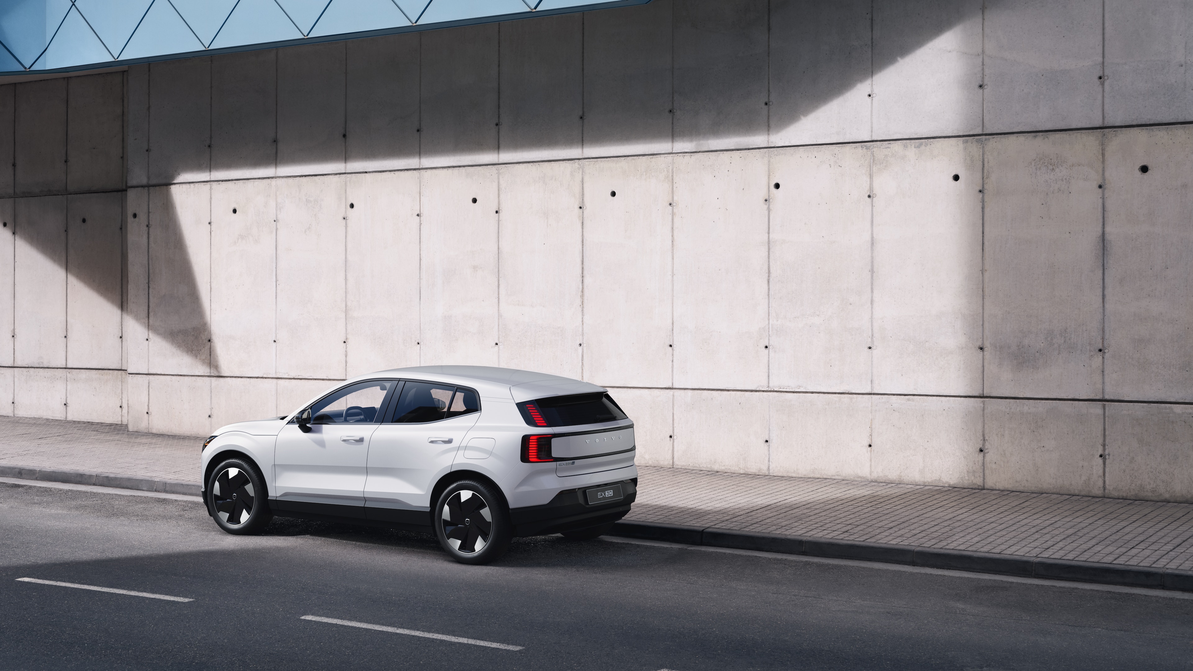 Volvo car in rear three-quarter view parked against a concrete wall on an urban street background.