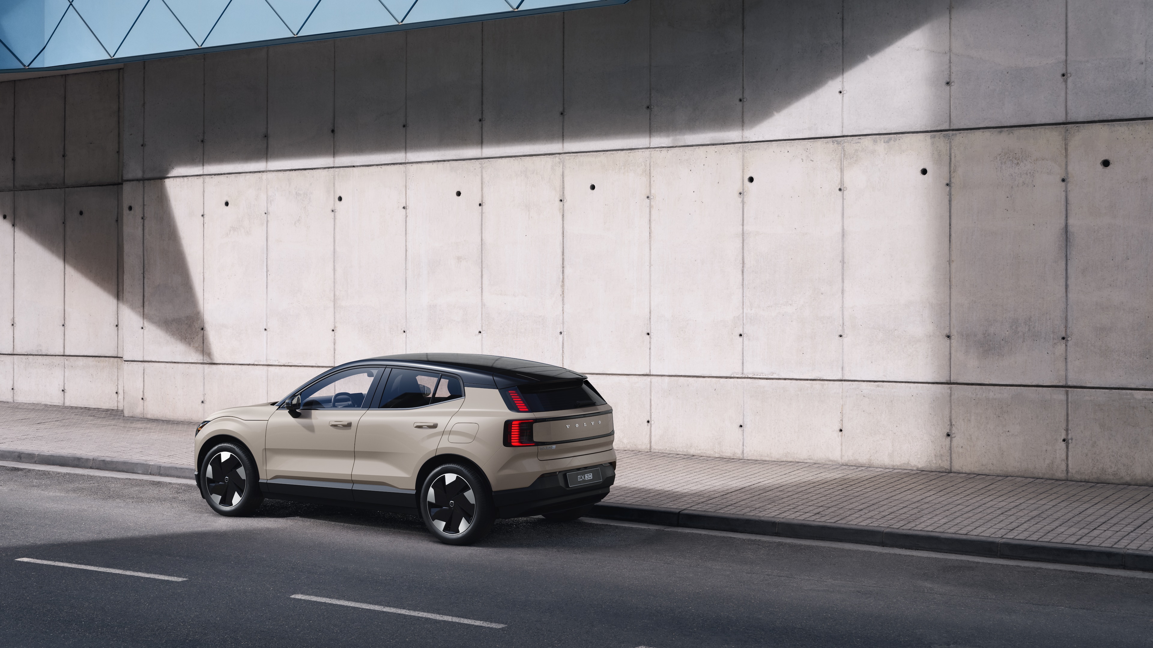 Volvo car in rear three-quarter view parked against a concrete wall on an urban street background.