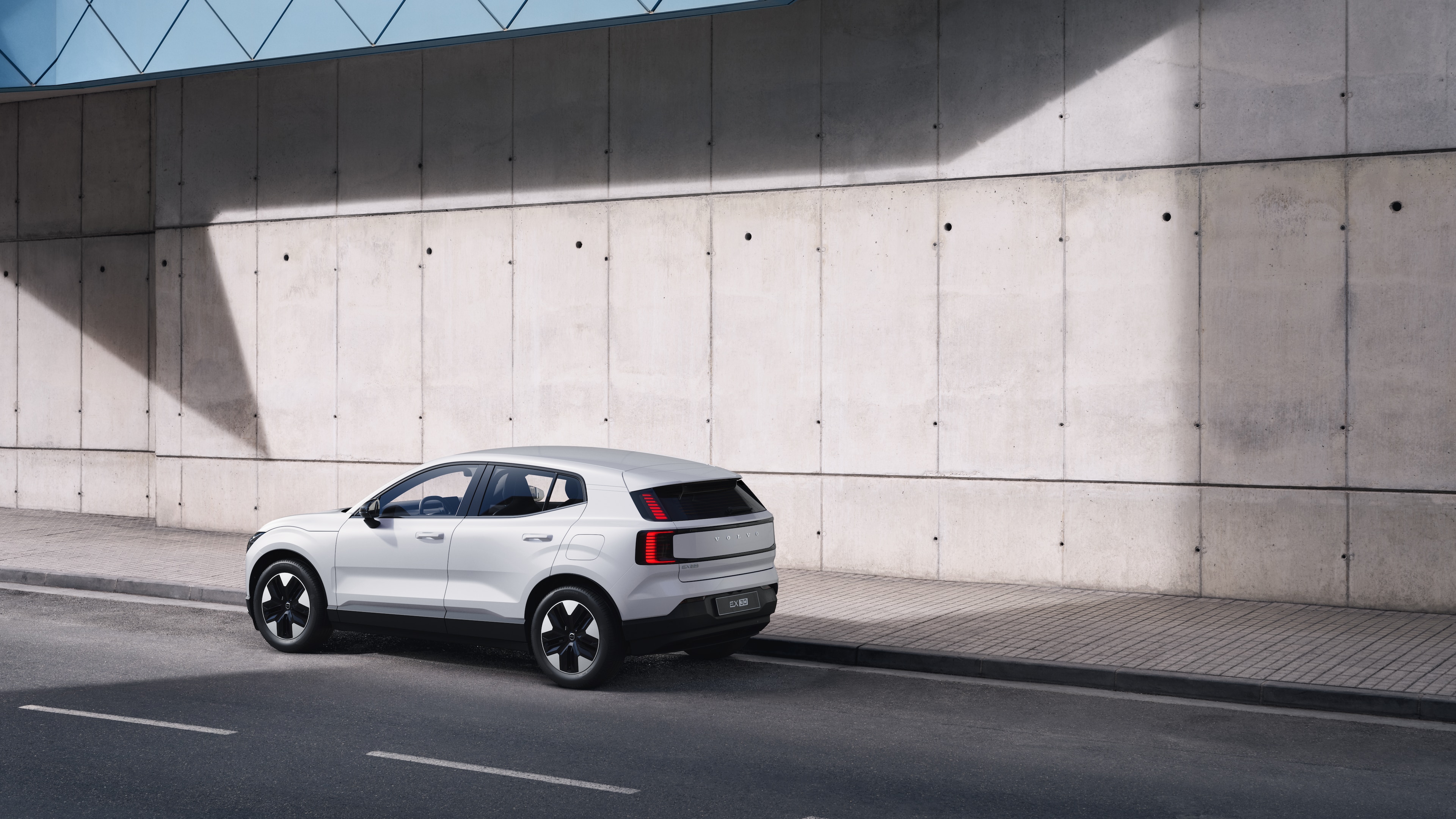 "Volvo" automobilis galiniame trijų ketvirčių vaizde, pastatytas priešais betoninę sieną miesto gatvės fone.