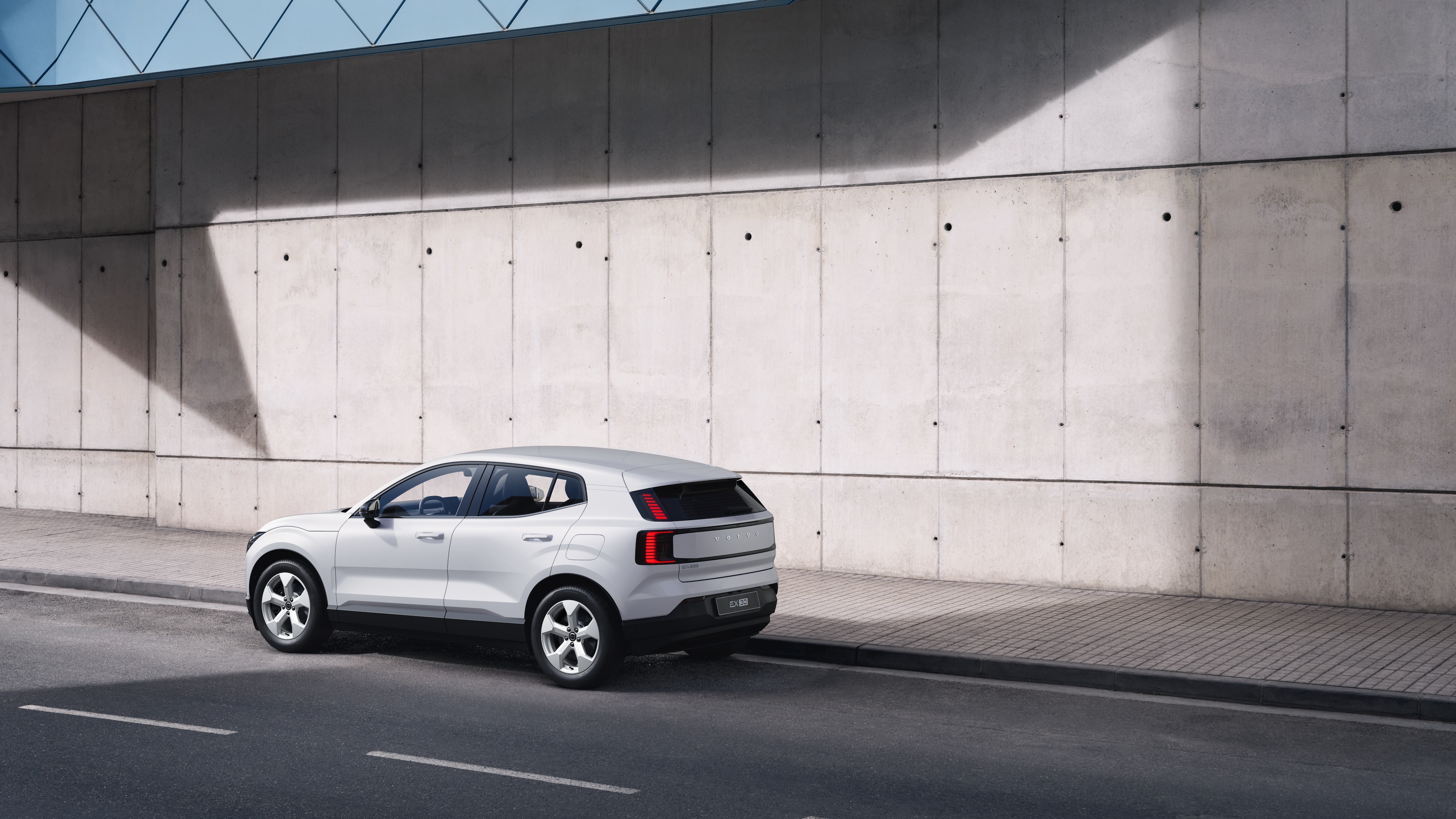 Vue arrière d’une Volvo de trois quarts, garée contre un mur de béton sur un fond de rue urbaine.