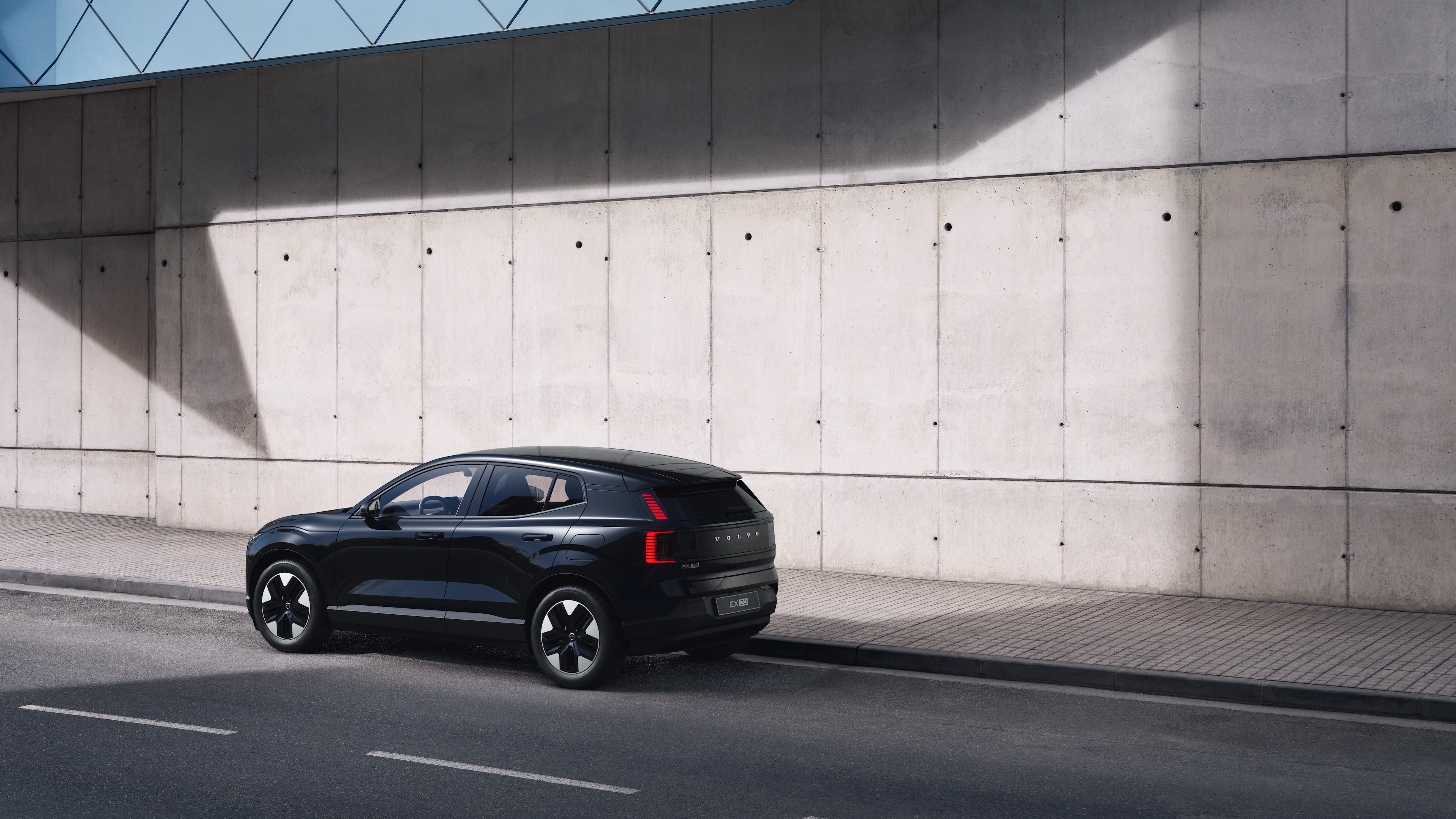 Driekwart achteraanzicht van een Volvo-auto geparkeerd tegen een betonnen muur op de achtergrond van een stedelijke straat.