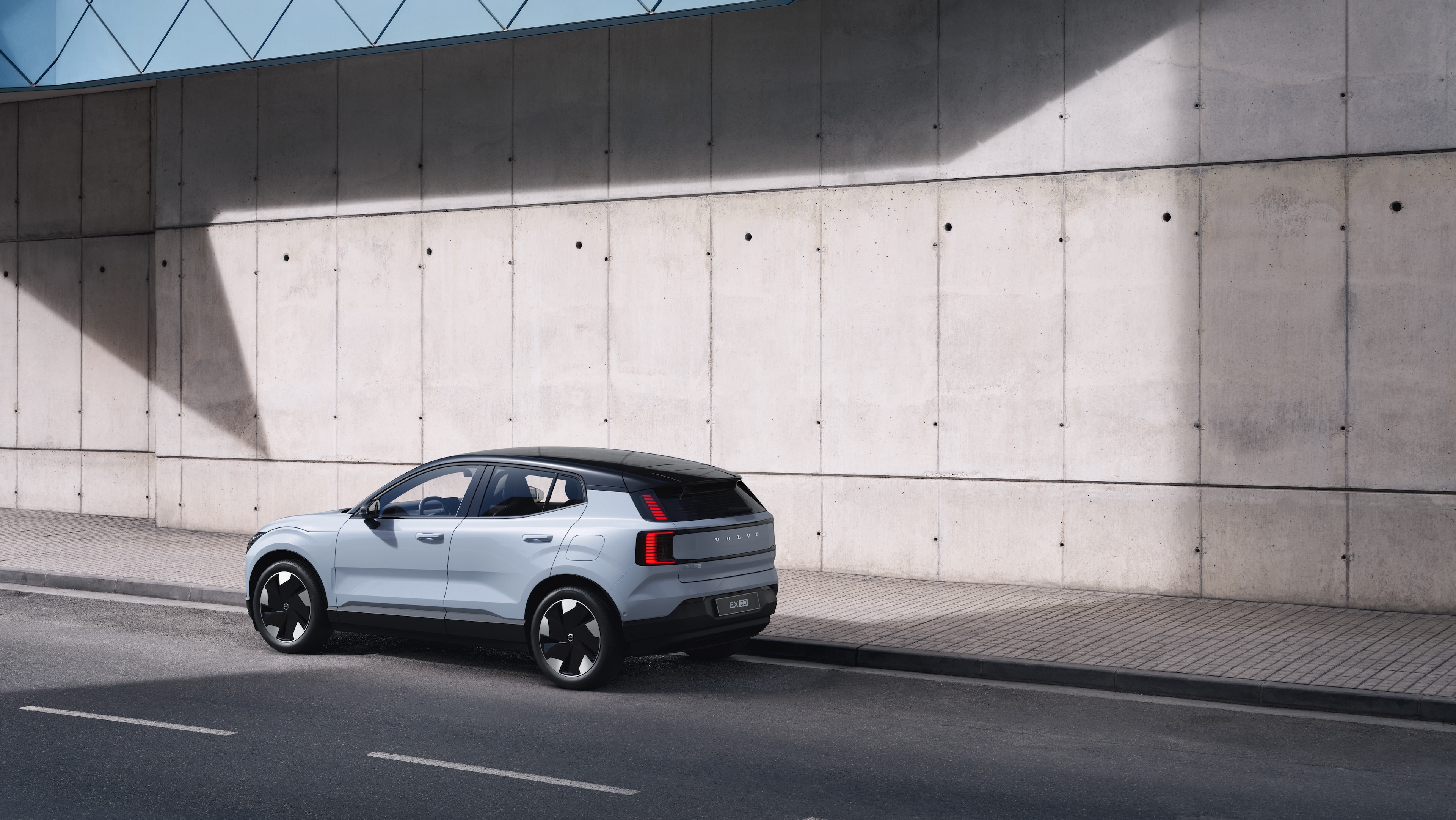 "Volvo" automobilis galiniame trijų ketvirčių vaizde, pastatytas priešais betoninę sieną miesto gatvės fone.