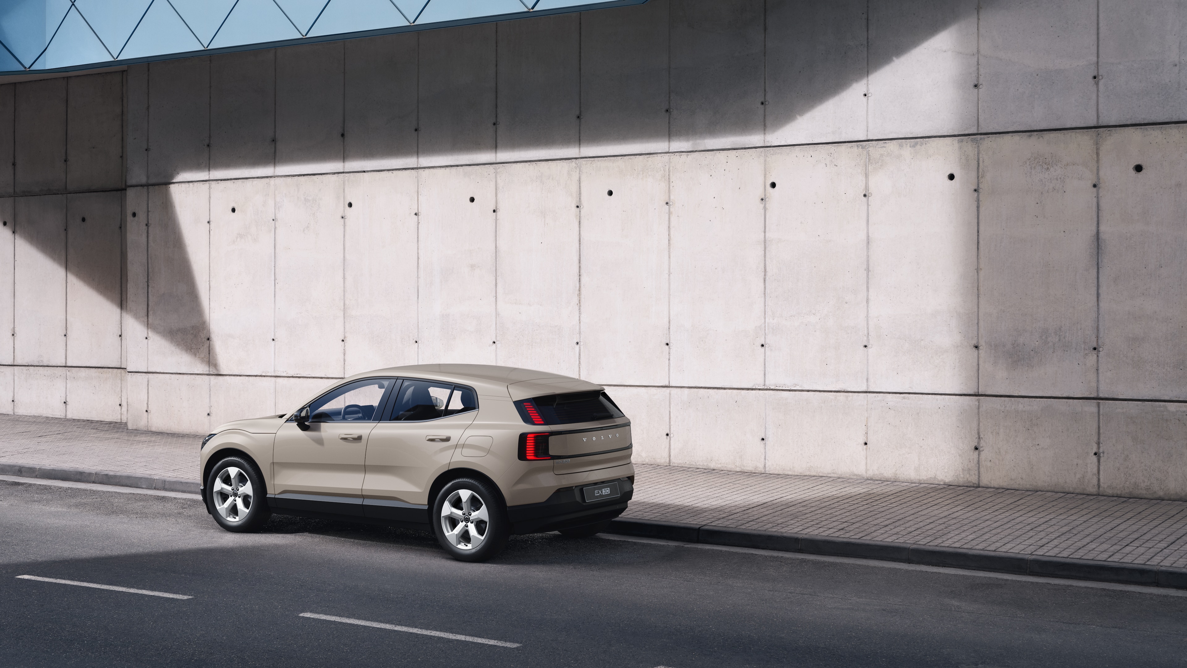 Coche Volvo en la parte trasera con vista de tres cuartos aparcado contra un muro de hormigón sobre el fondo de una calle urbana.