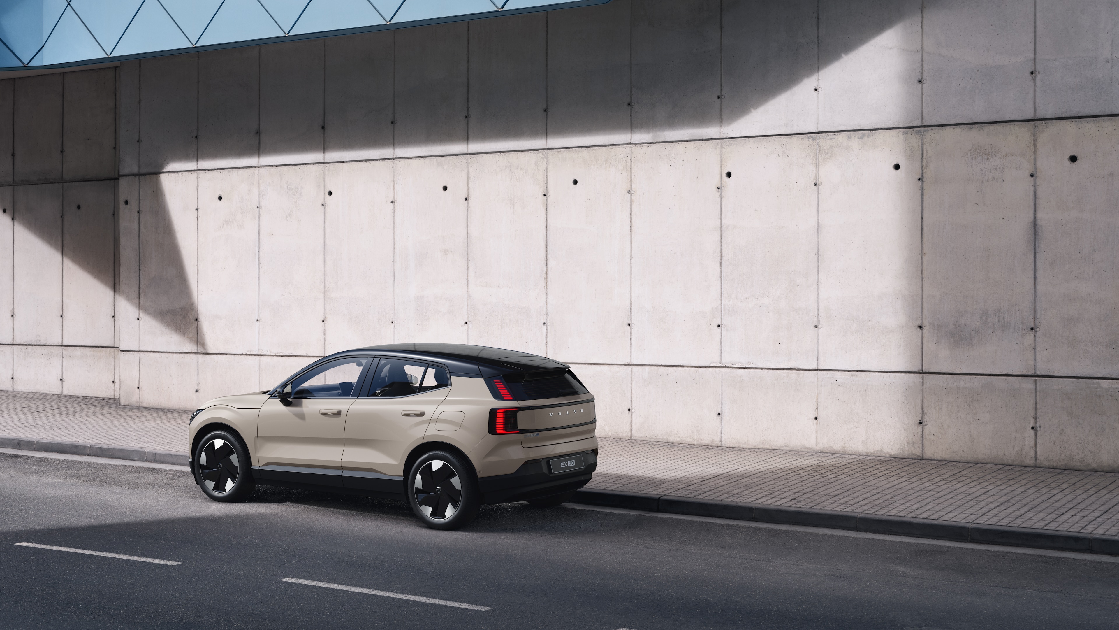 Volvo car in rear three-quarter view parked against a concrete wall on an urban street background.
