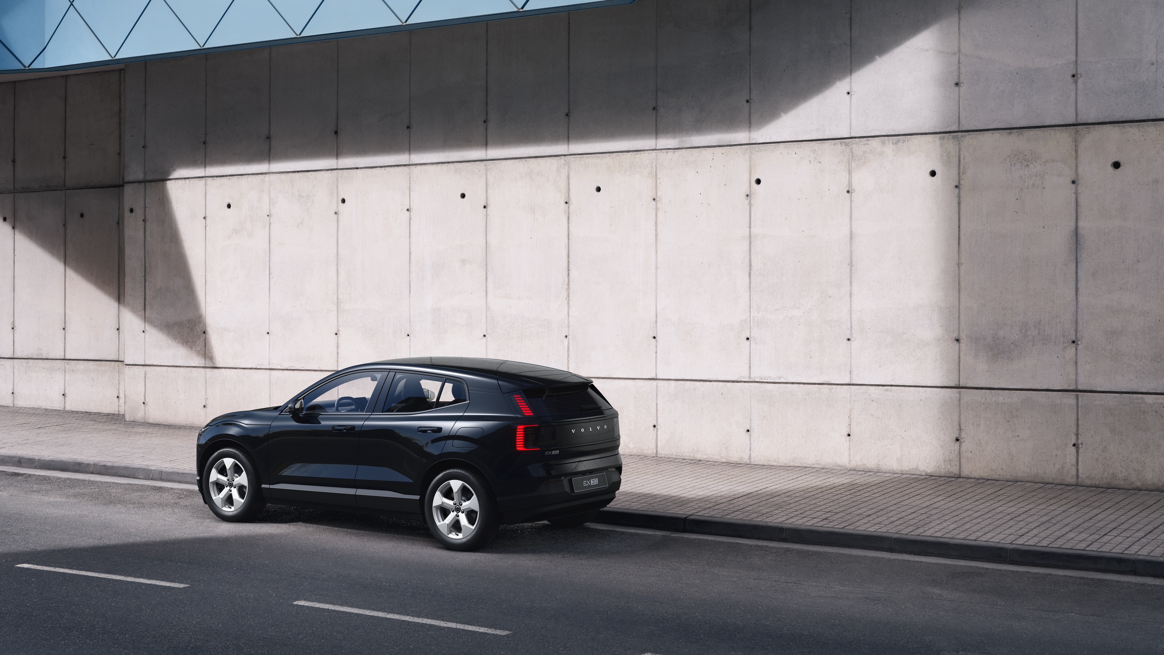 Vue arrière d’une Volvo de trois quarts, garée contre un mur de béton sur un fond de rue urbaine.