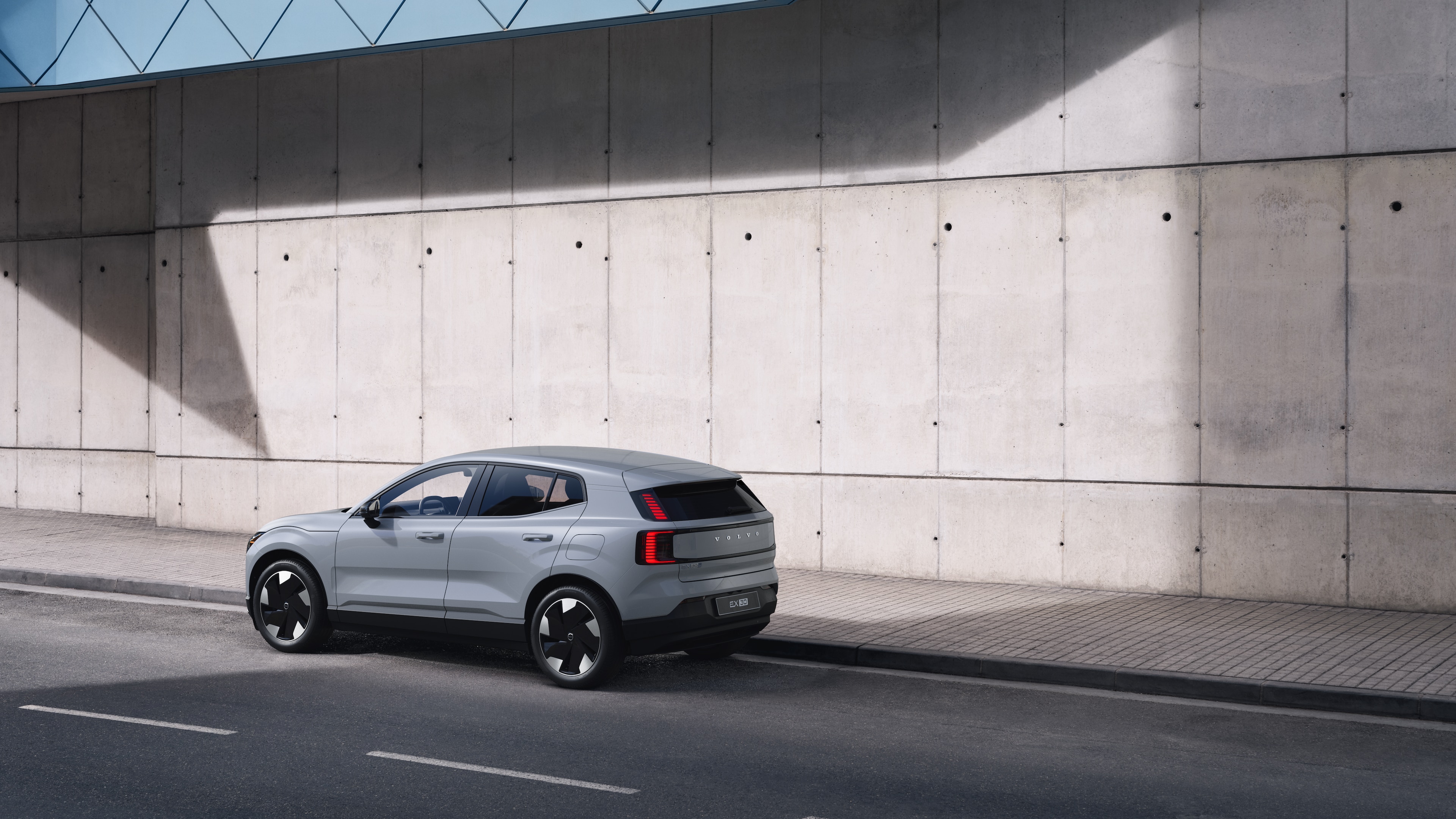 Voiture Volvo en vue arrière de trois quarts, garée contre un mur en béton sur un fond de rue urbaine.