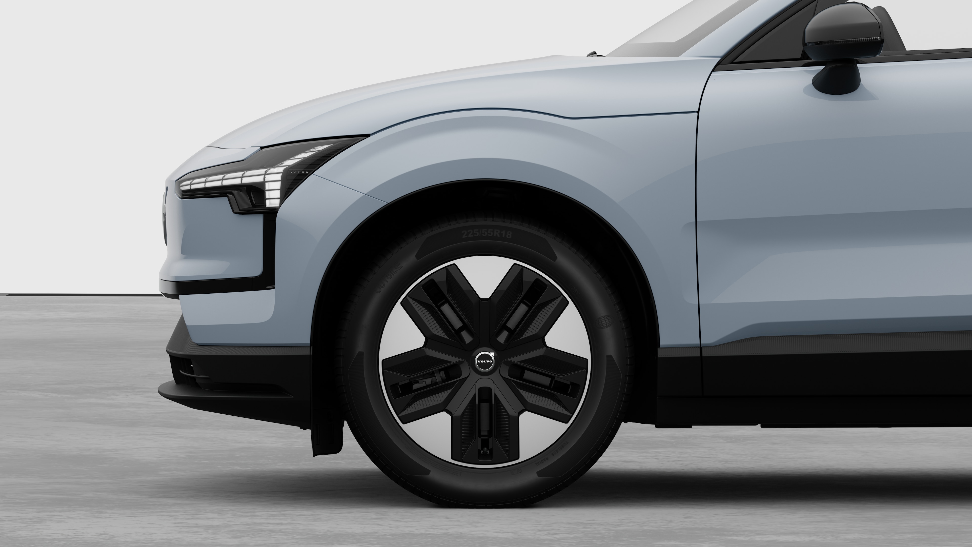 Екстериорен страничен изглед на автомобил Volvo, фокусиран върху предното колело и калника, поставен на обикновен студиен фон.