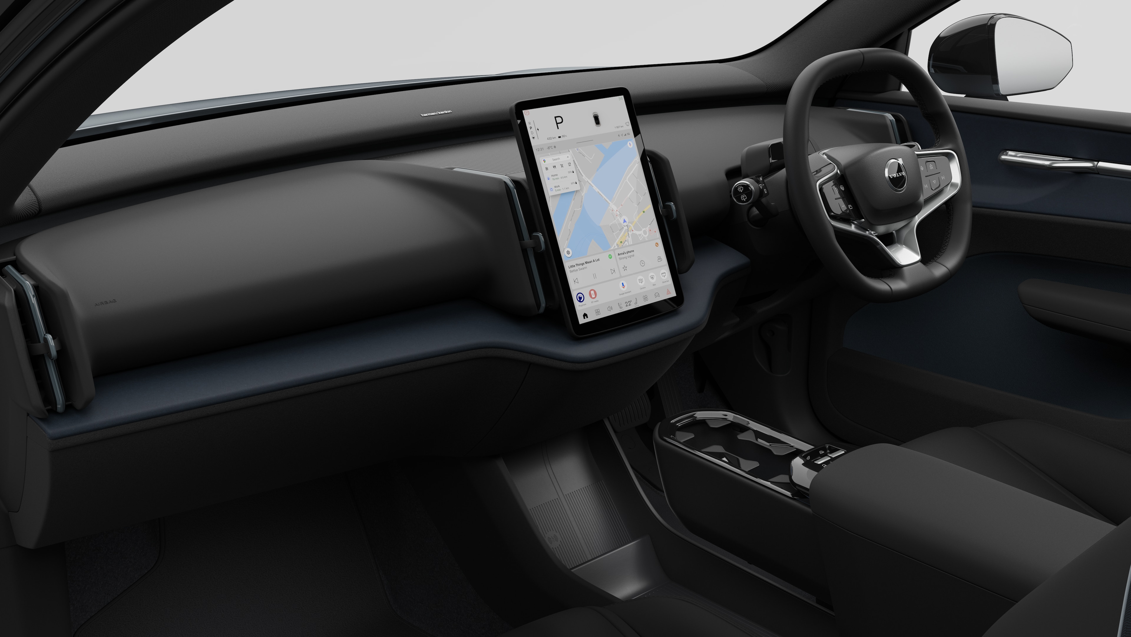 Interior view of a Volvo car showing the dashboard, steering wheel, center console, and digital display screen in a plain studio background.