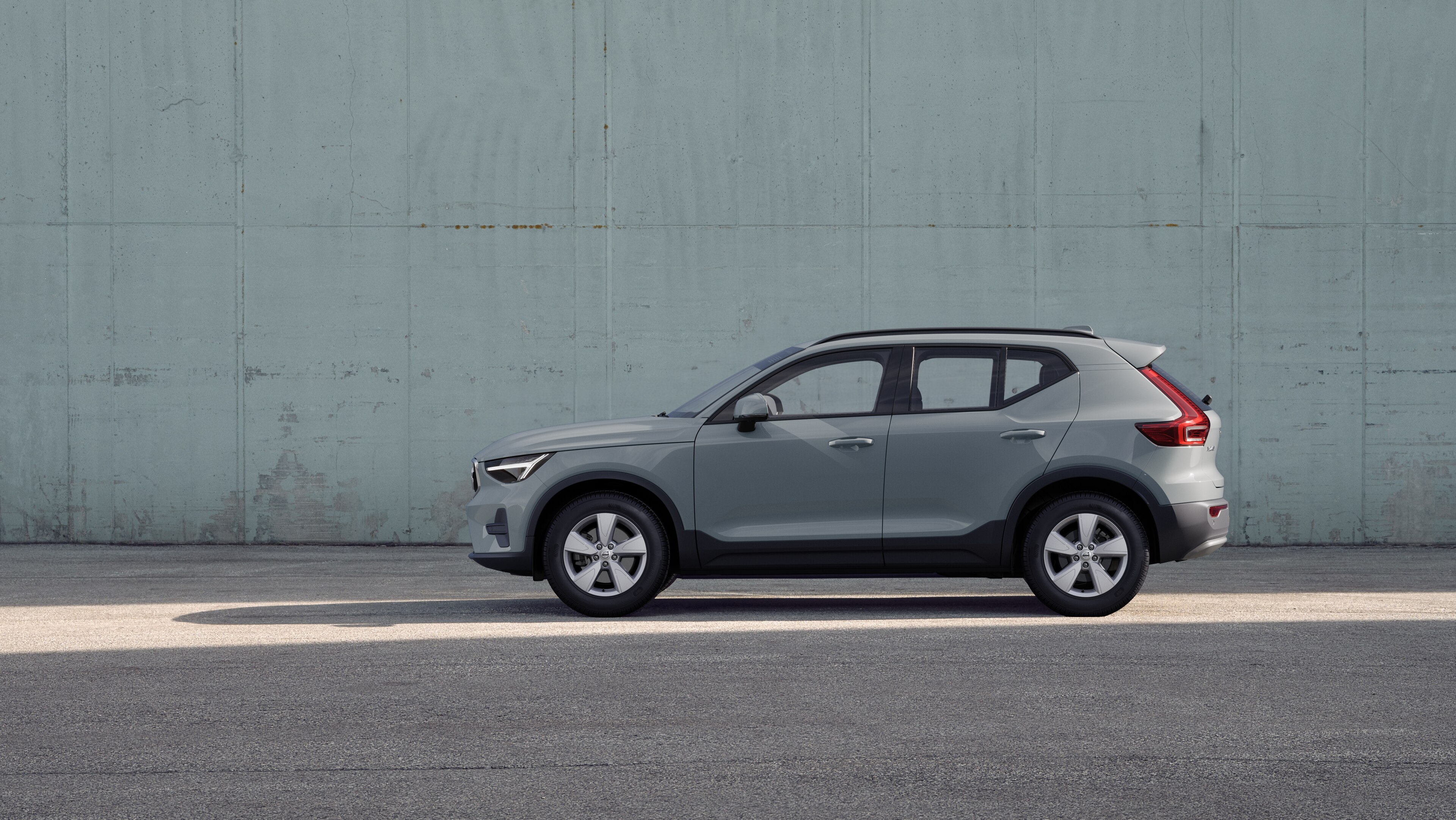 Volvo, zijaanzicht, geparkeerd tegen een effen betonnen muurachtergrond.