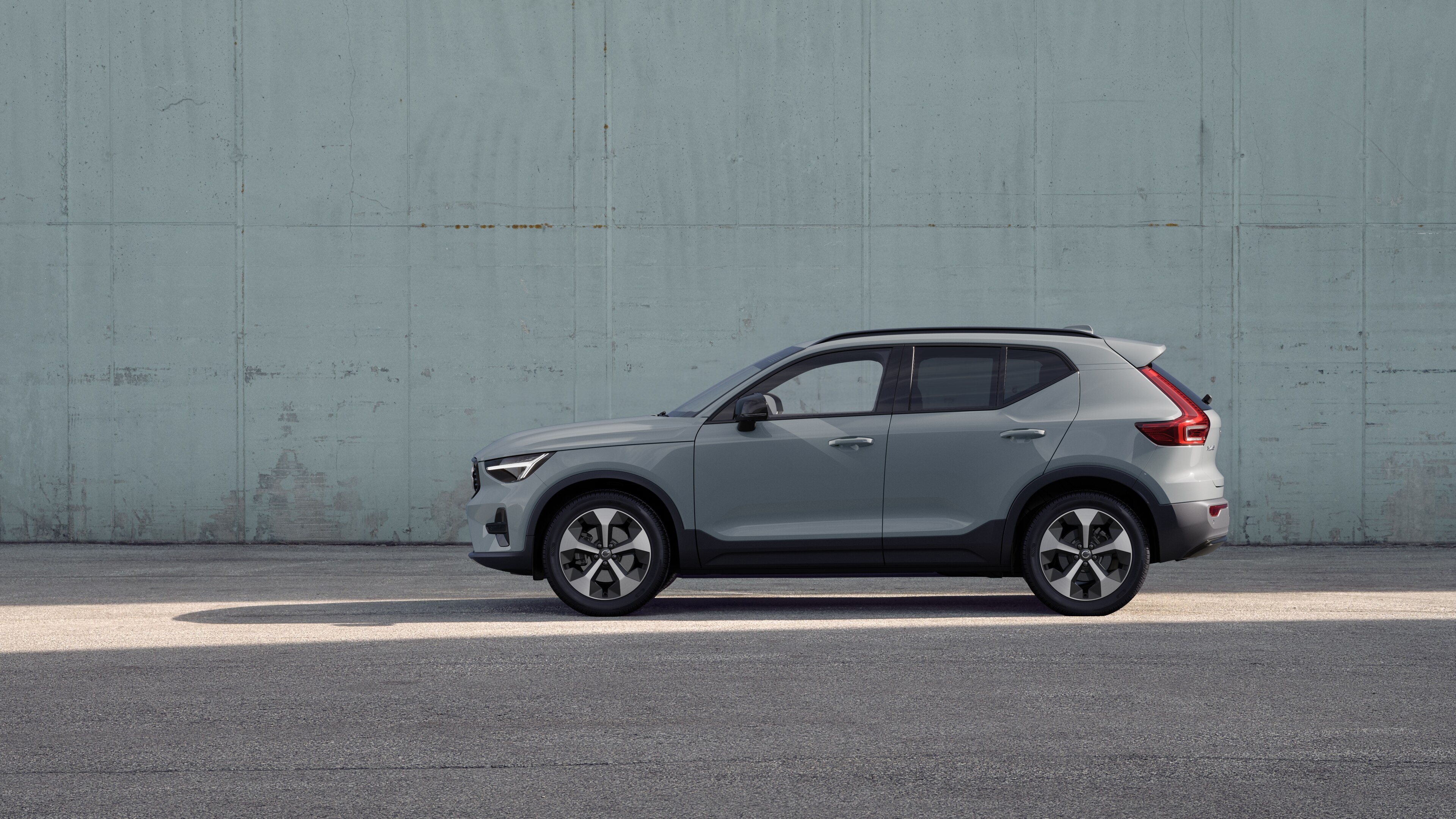 Volvo, zijaanzicht, geparkeerd tegen een effen betonnen muurachtergrond.