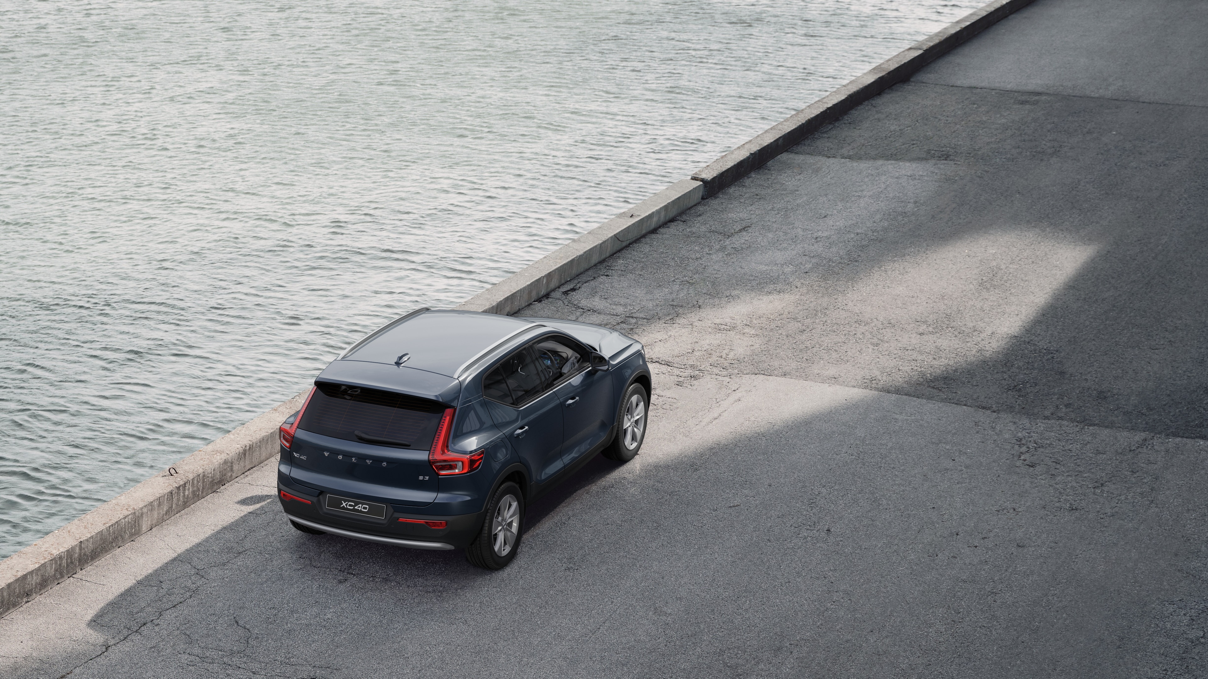 Volvo car rear view parked on quiet street beside water, with a paved walkway and water as the background.