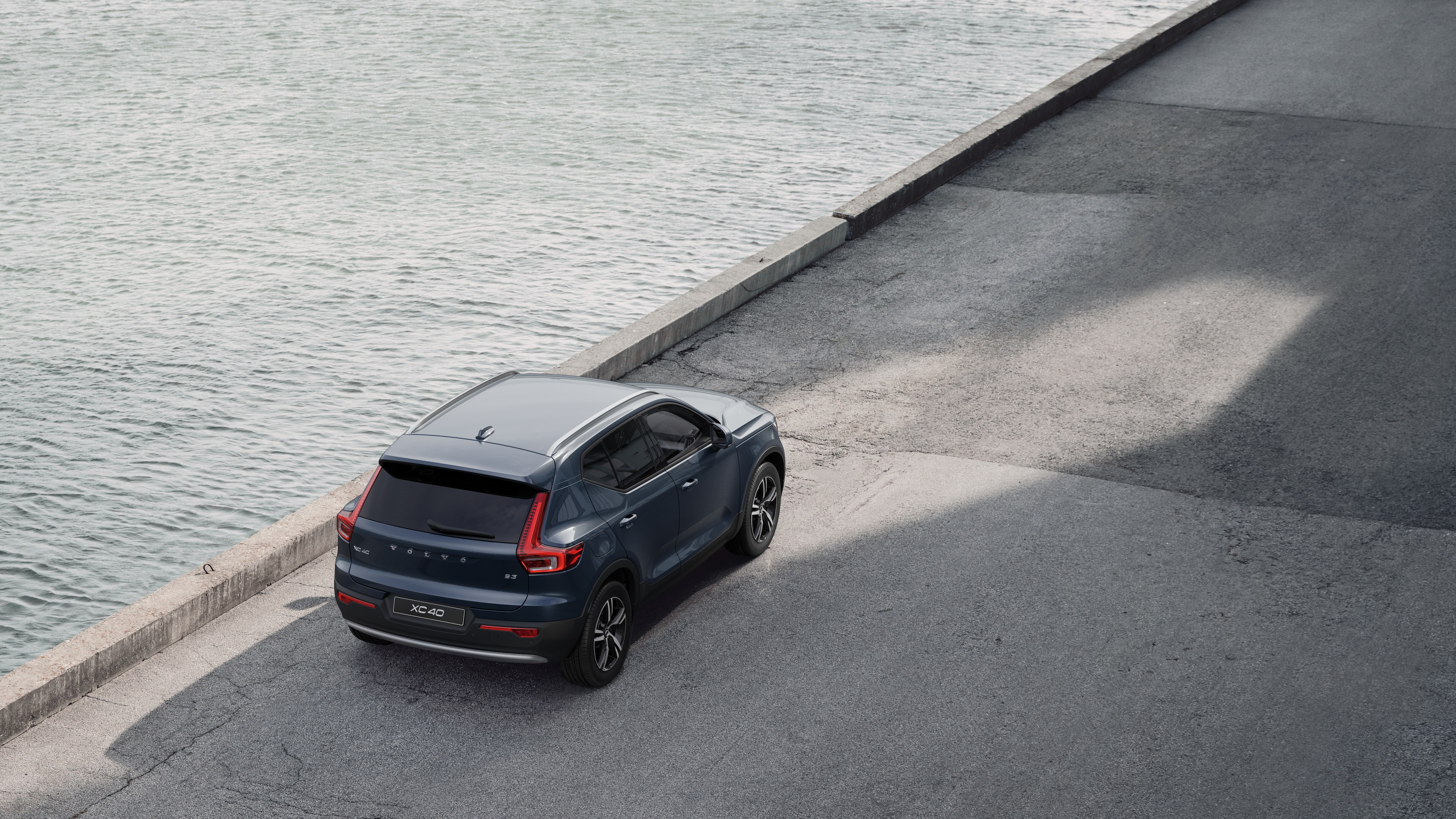 Achteraanzicht van een Volvo geparkeerd in een rustige straat naast water, met een verharde loopbrug en water op de achtergrond.