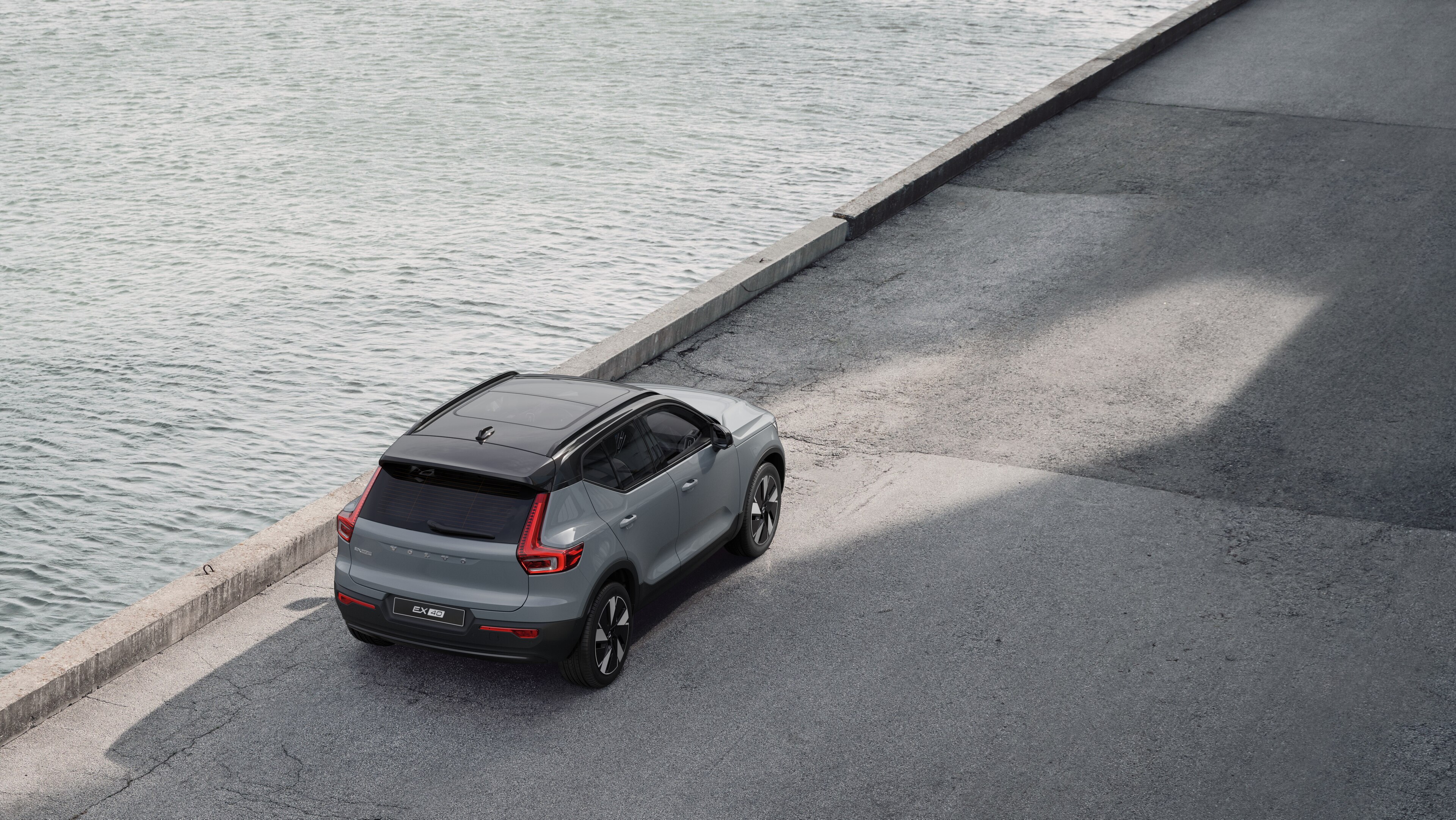 Vue arrière d’une Volvo garée dans une rue calme au bord de l’eau, avec une passerelle pavée et de l’eau en arrière-plan.