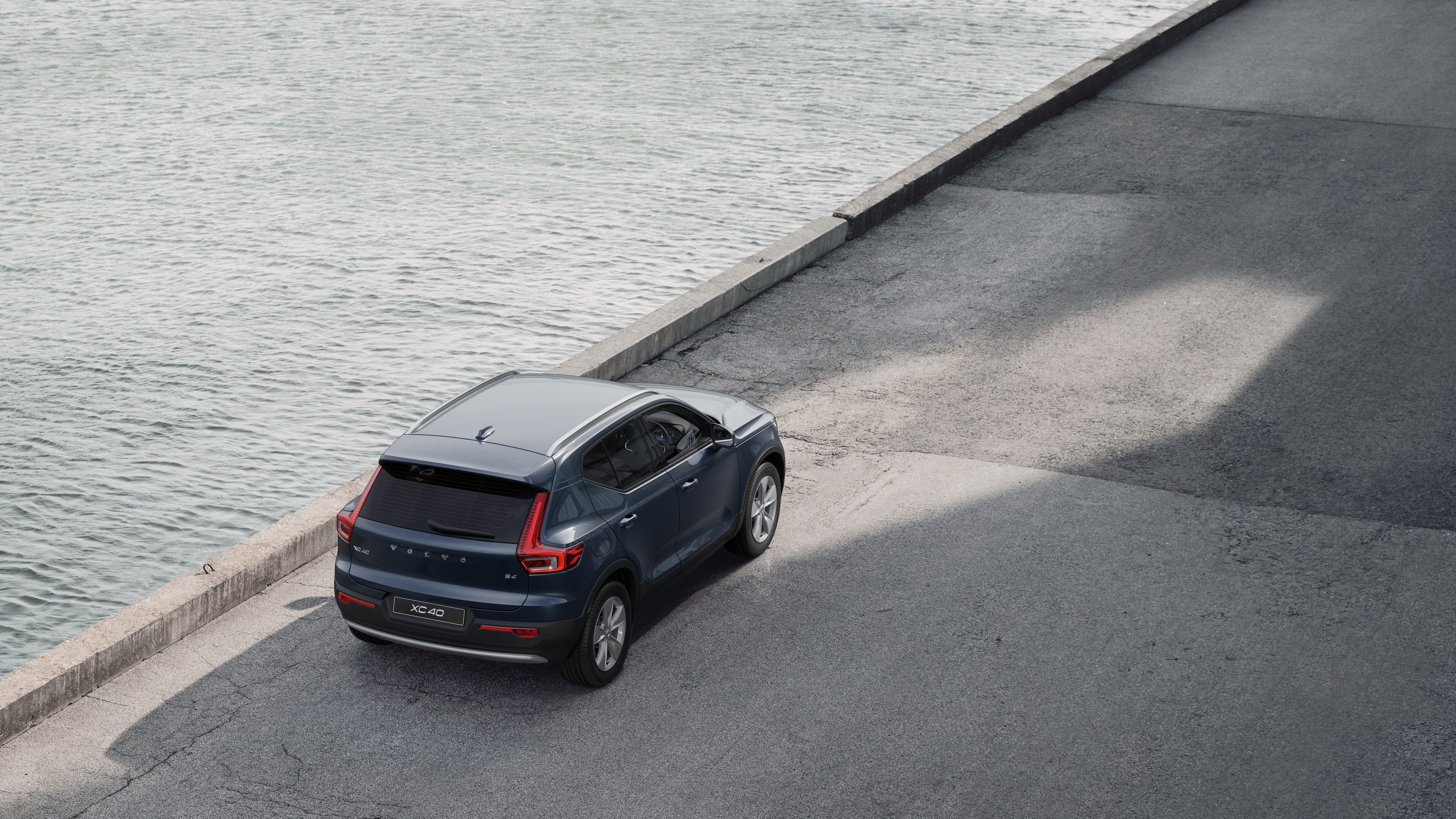 Volvo car rear view parked on quiet street beside water, with a paved walkway and water as the background.