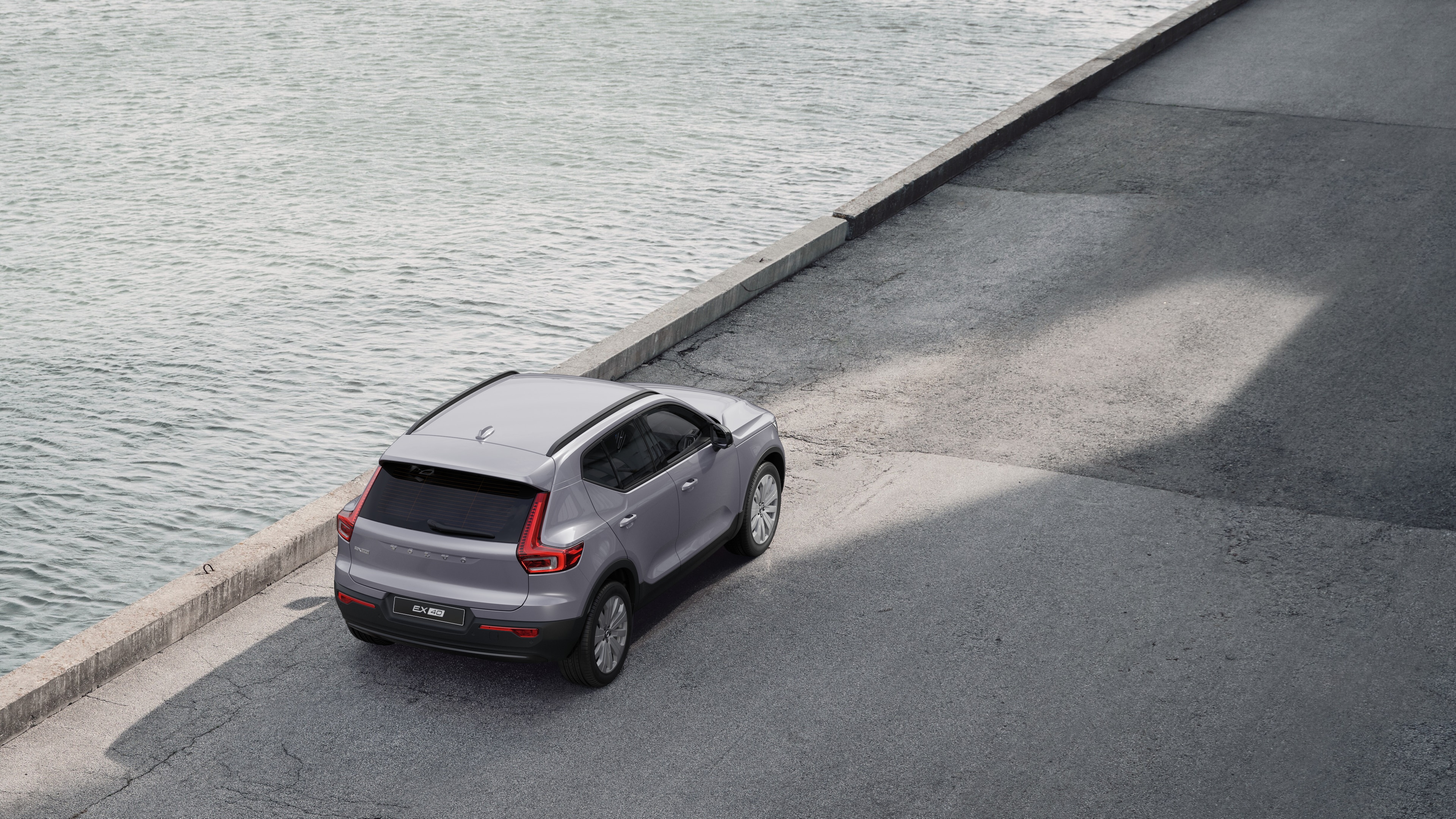 Volvo-bil set bagfra parkeret på en stille gade ved siden af vandet med en asfalteret gangbro og vand som baggrund.