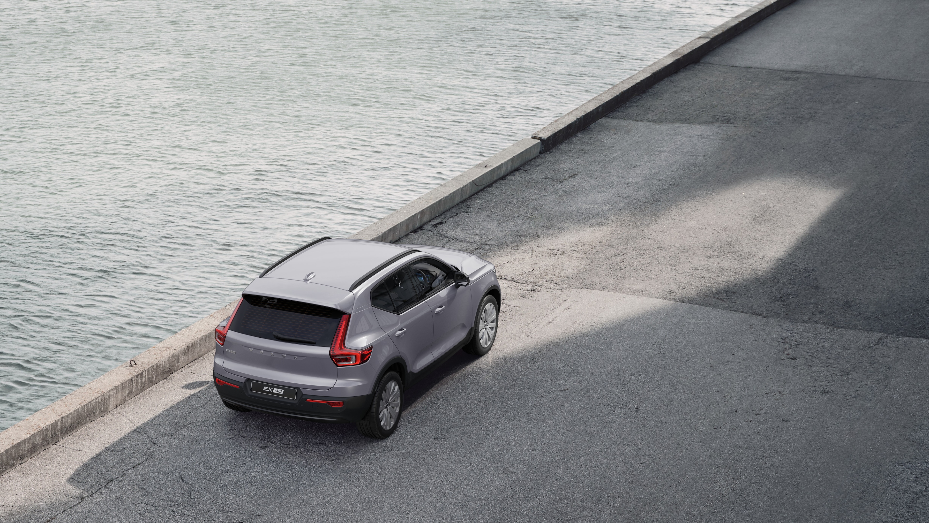 Volvo car rear view parked on quiet street beside water, with a paved walkway and water as the background.