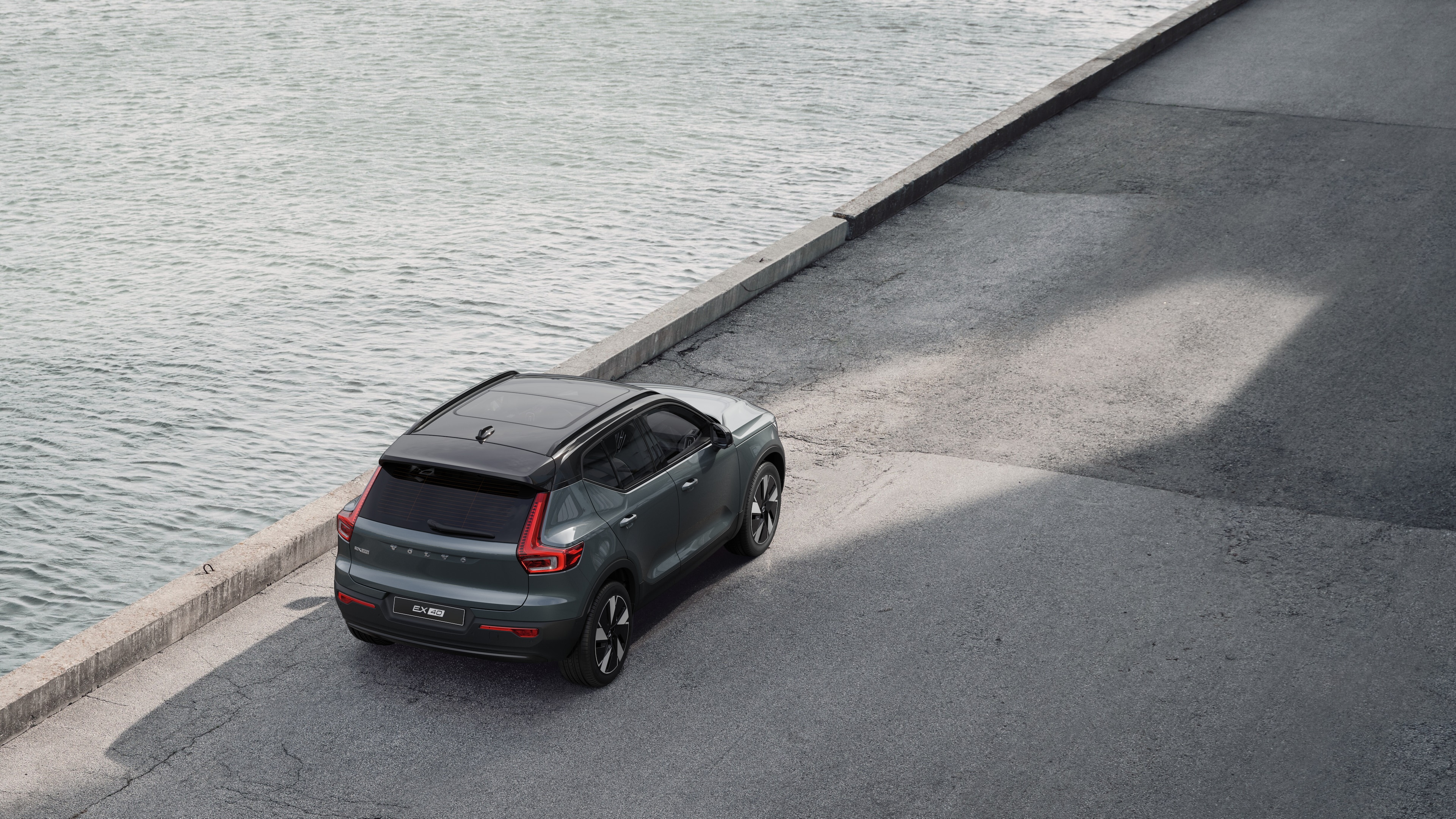 Volvo avtomobilinin arxa görünüşü suyun yanında sakit küçədə dayanmışdı. Arxa fon kimi döşənmiş piyada və su var idi.