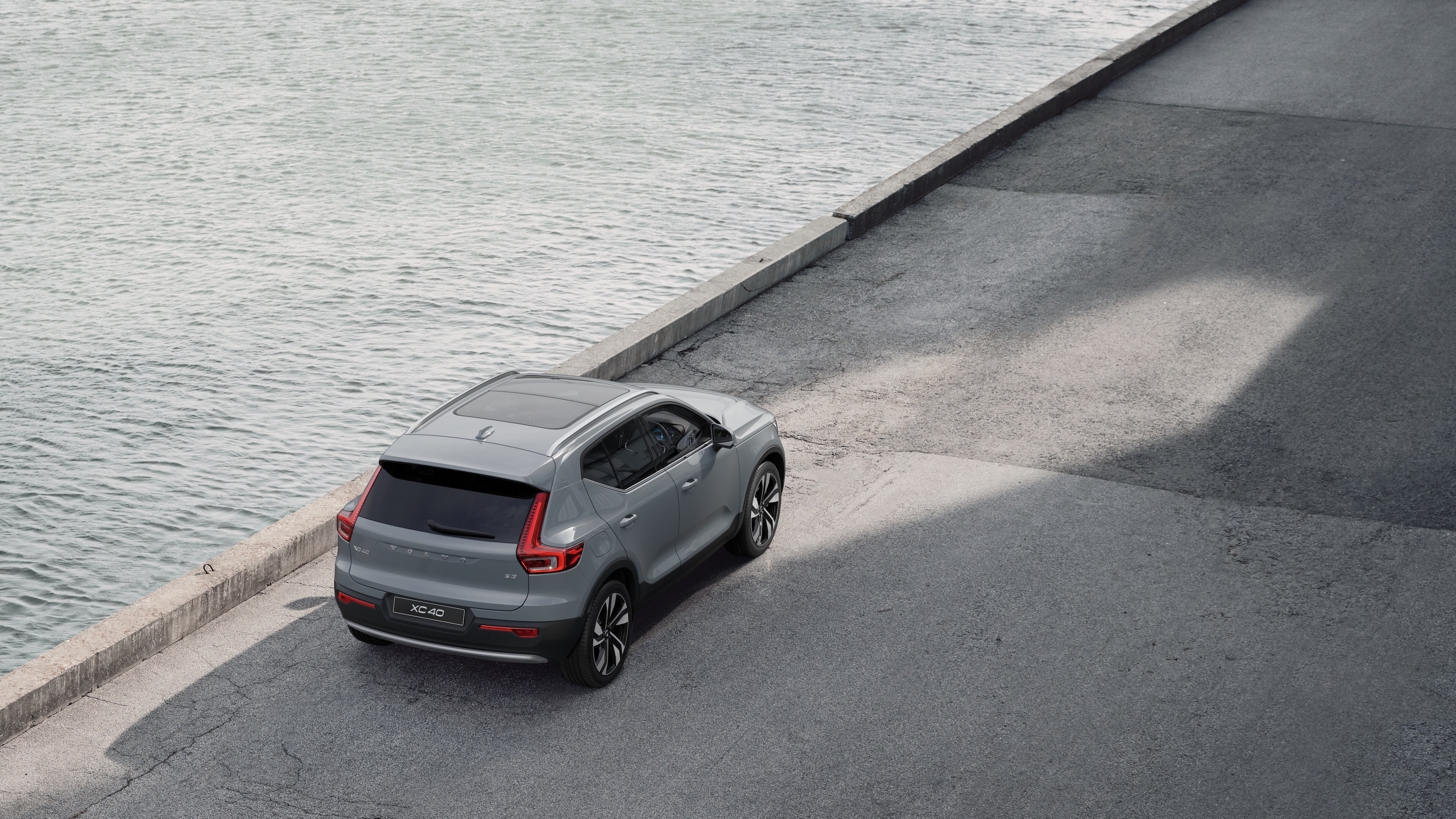 Volvo car rear view parked on quiet street beside water, with a paved walkway and water as the background.