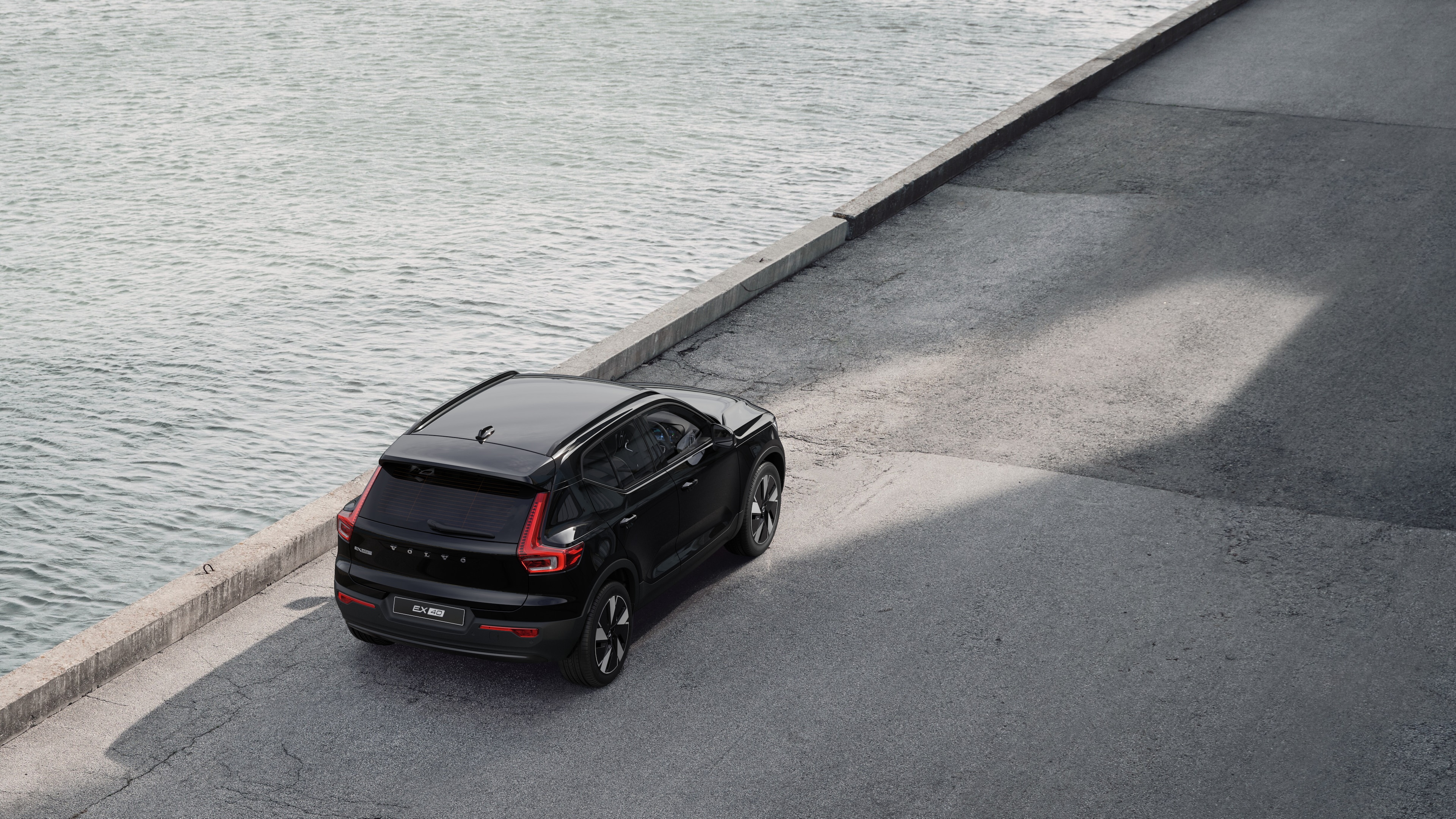 Volvo car rear view parked on quiet street beside water, with a paved walkway and water as the background.