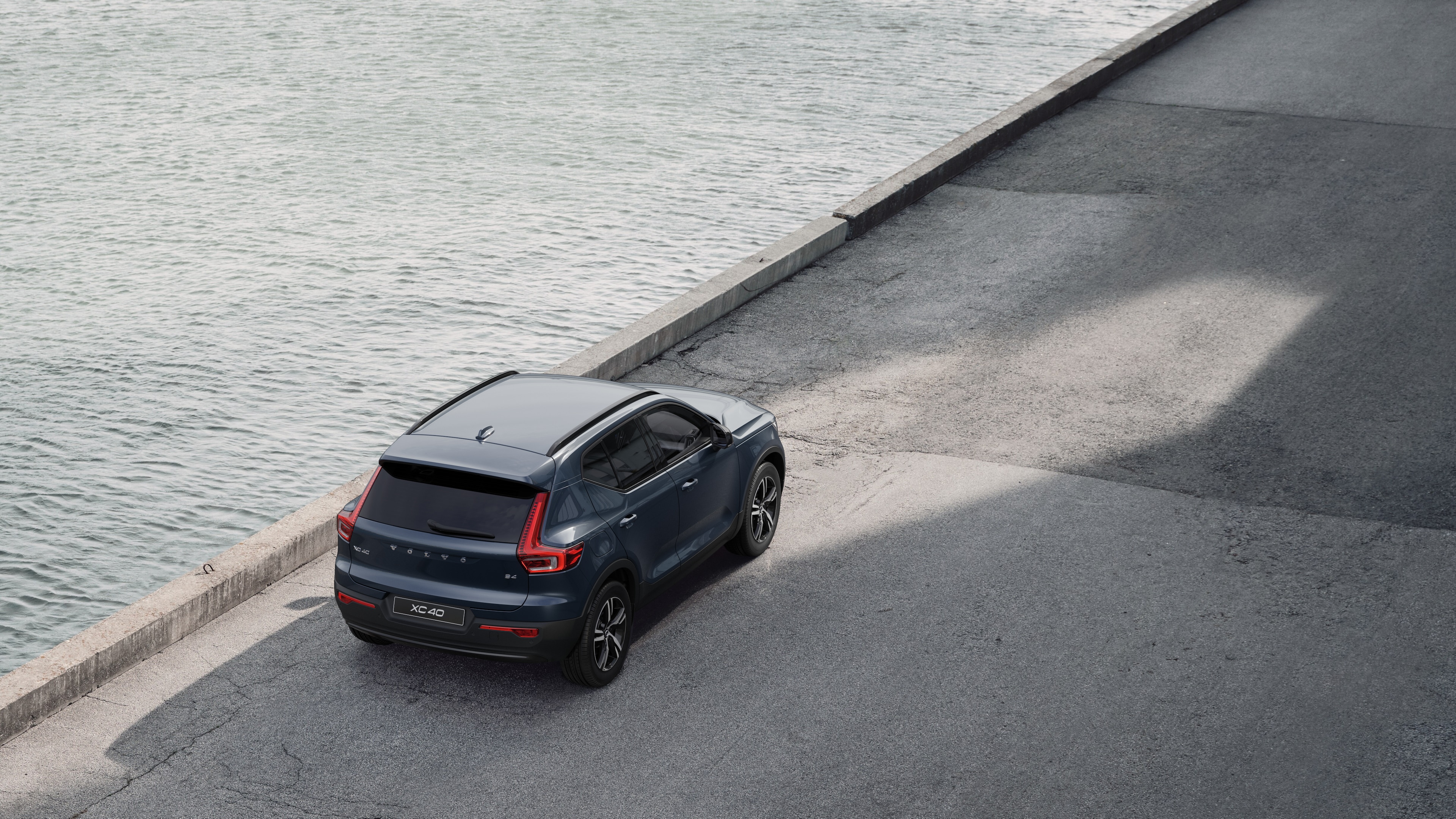 Volvo car rear view parked on quiet street beside water, with a paved walkway and water as the background.