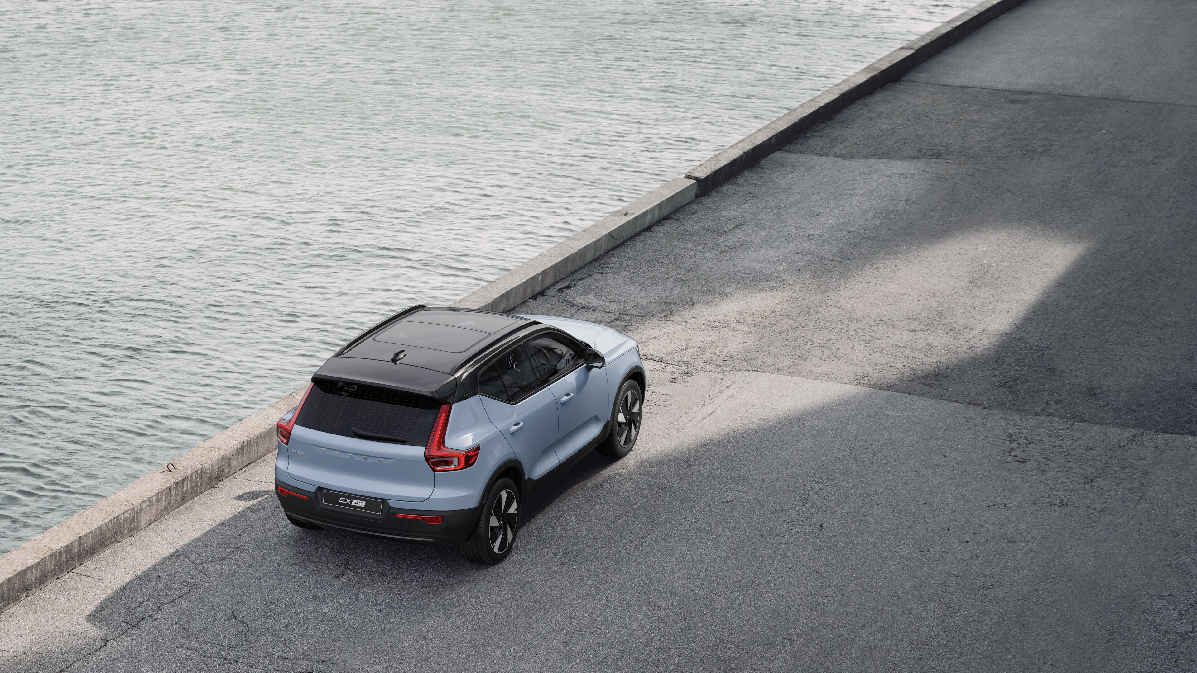 Volvo car rear view parked on quiet street beside water, with a paved walkway and water as the background.