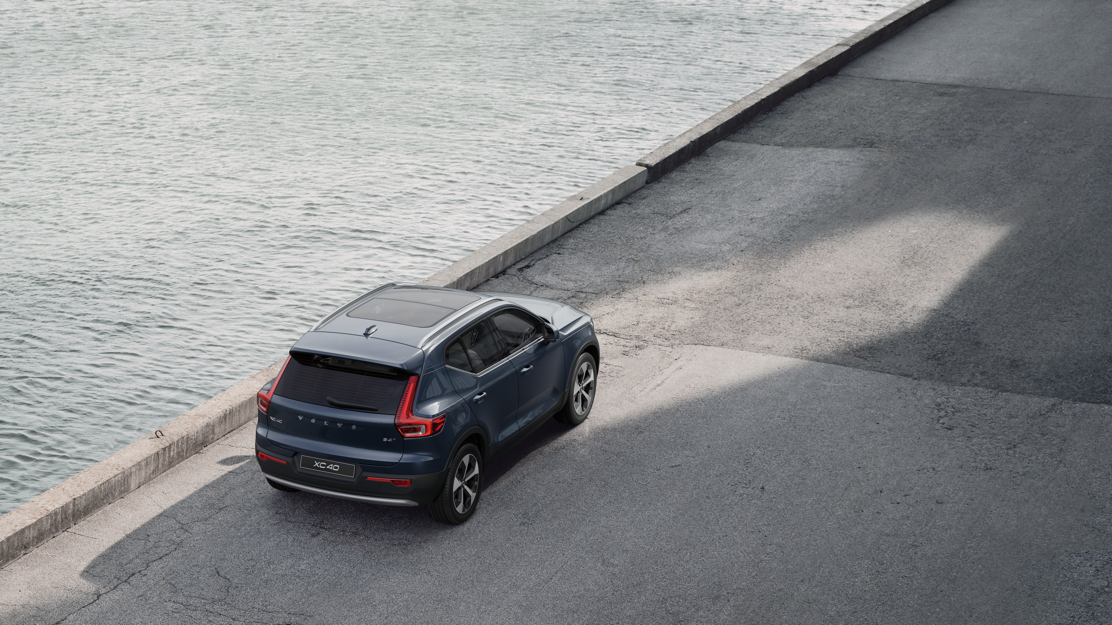 물가의 조용한 거리에 주차된 볼보 자동차 후면도, 포장된 보도와 물을 배경으로 합니다.