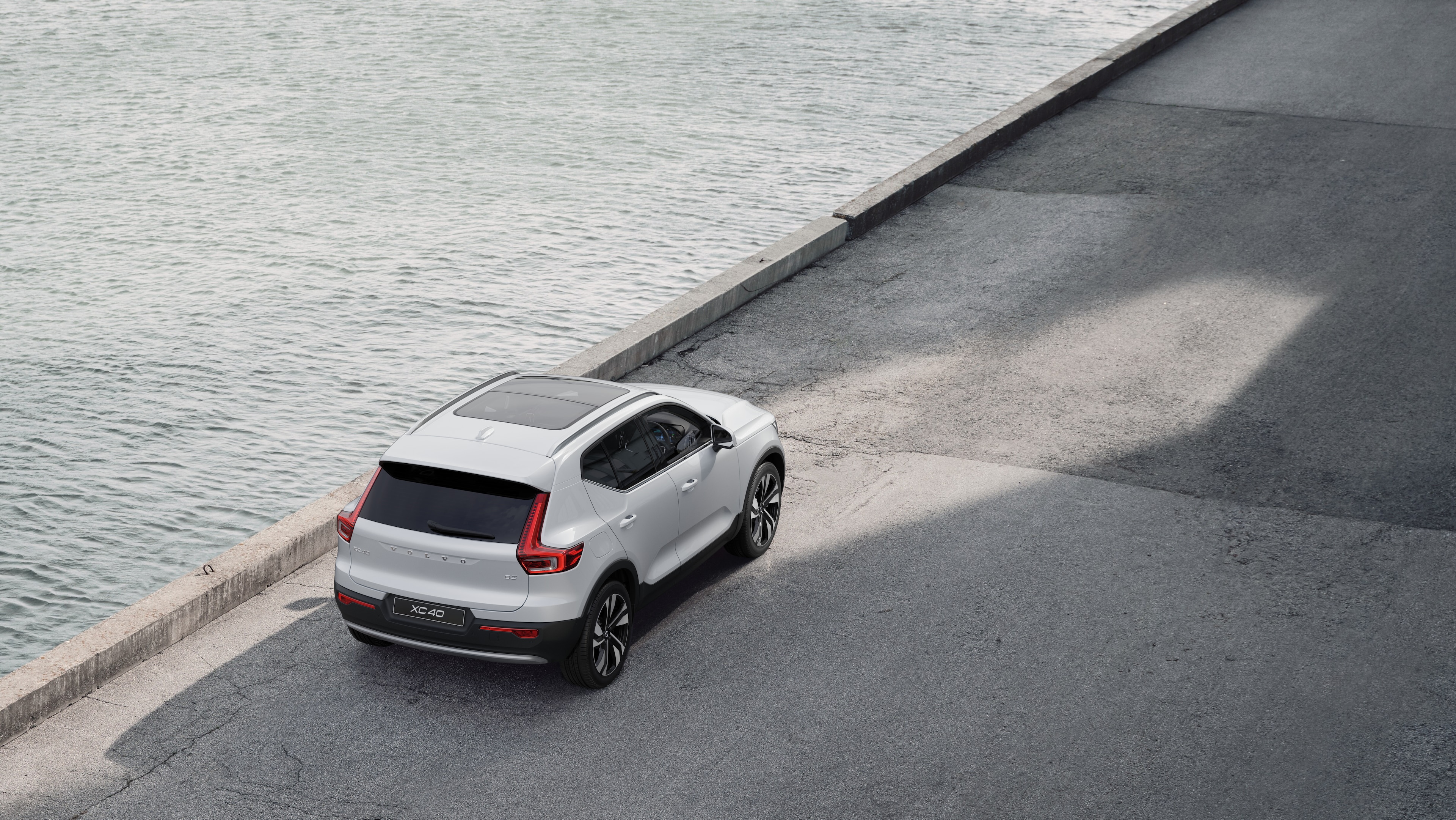 Volvo car rear view parked on quiet street beside water, with a paved walkway and water as the background.