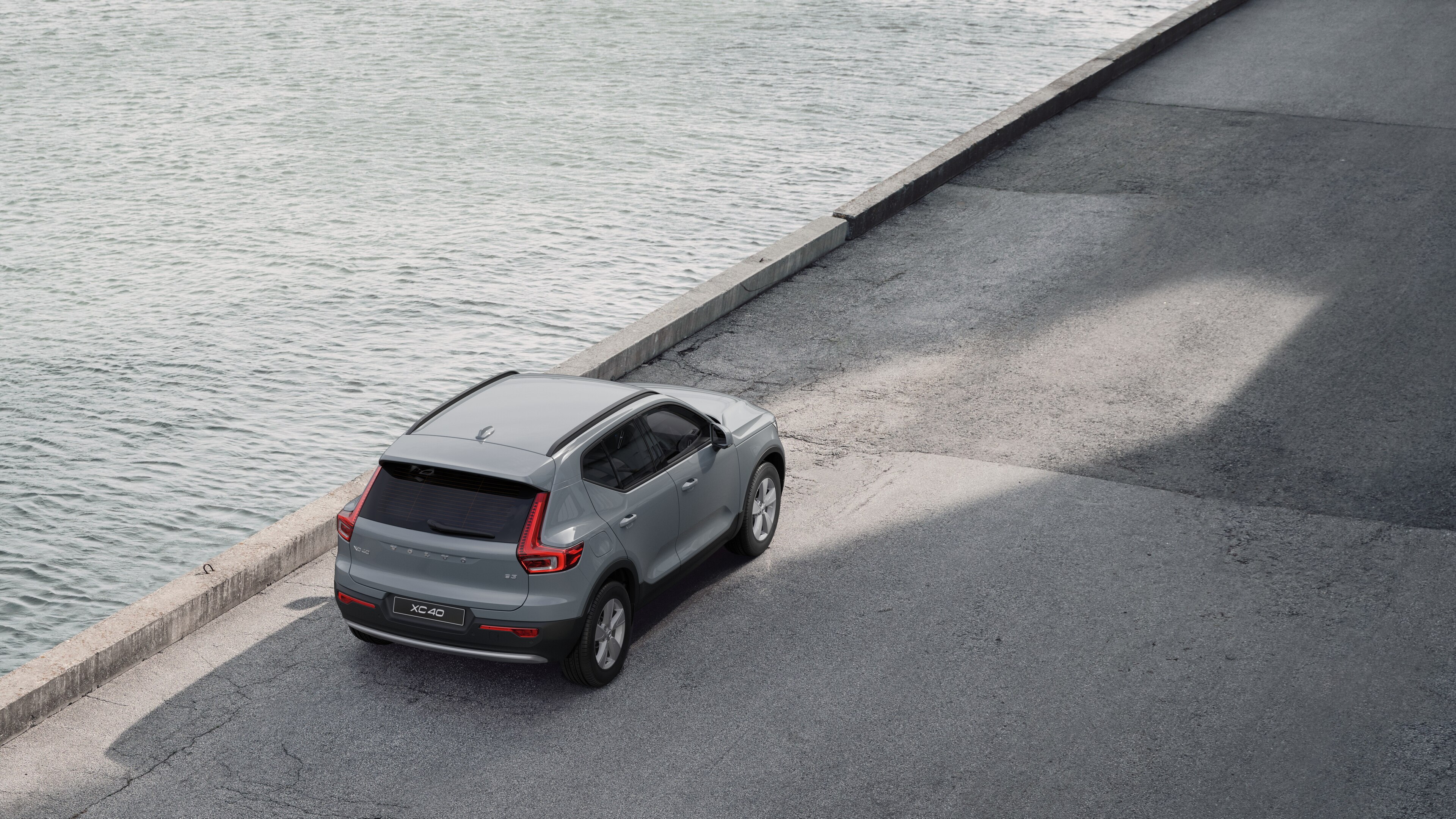 Achteraanzicht van een Volvo geparkeerd in een rustige straat aan het water, met een geplaveid looppad en water als achtergrond.