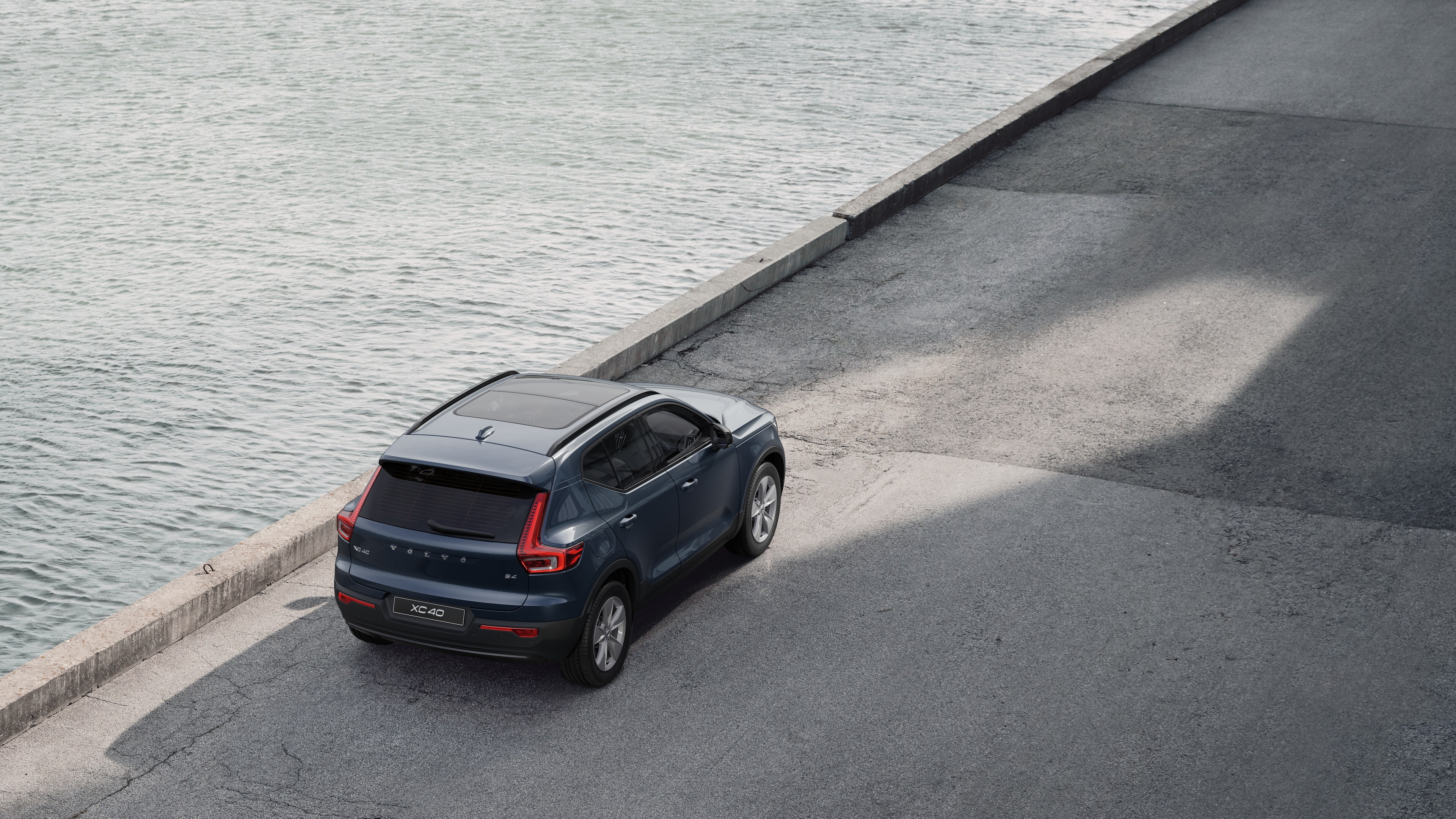 Volvo car rear view parked on quiet street beside water, with a paved walkway and water as the background.