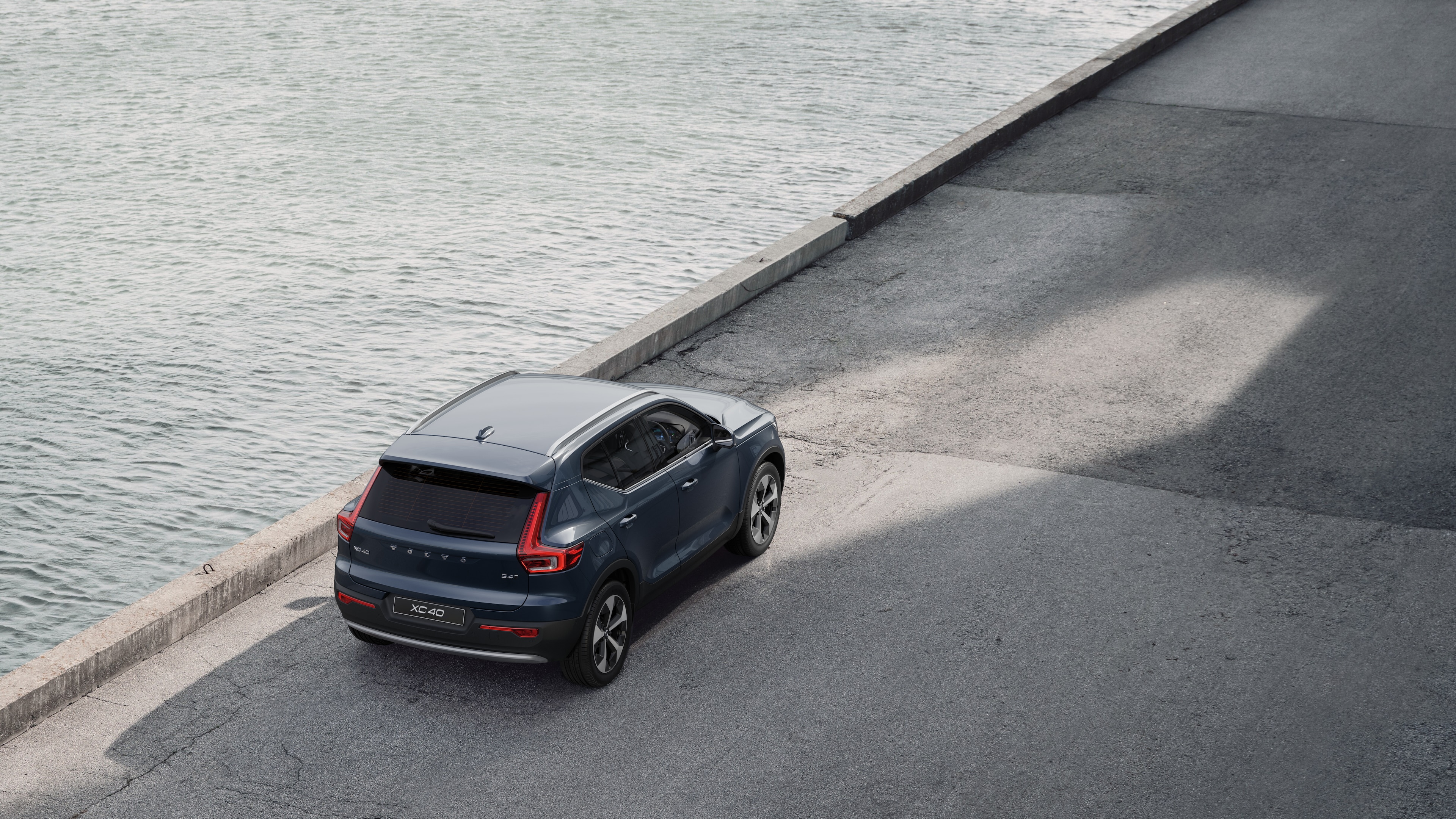 Volvo car rear view parked on quiet street beside water, with a paved walkway and water as the background.