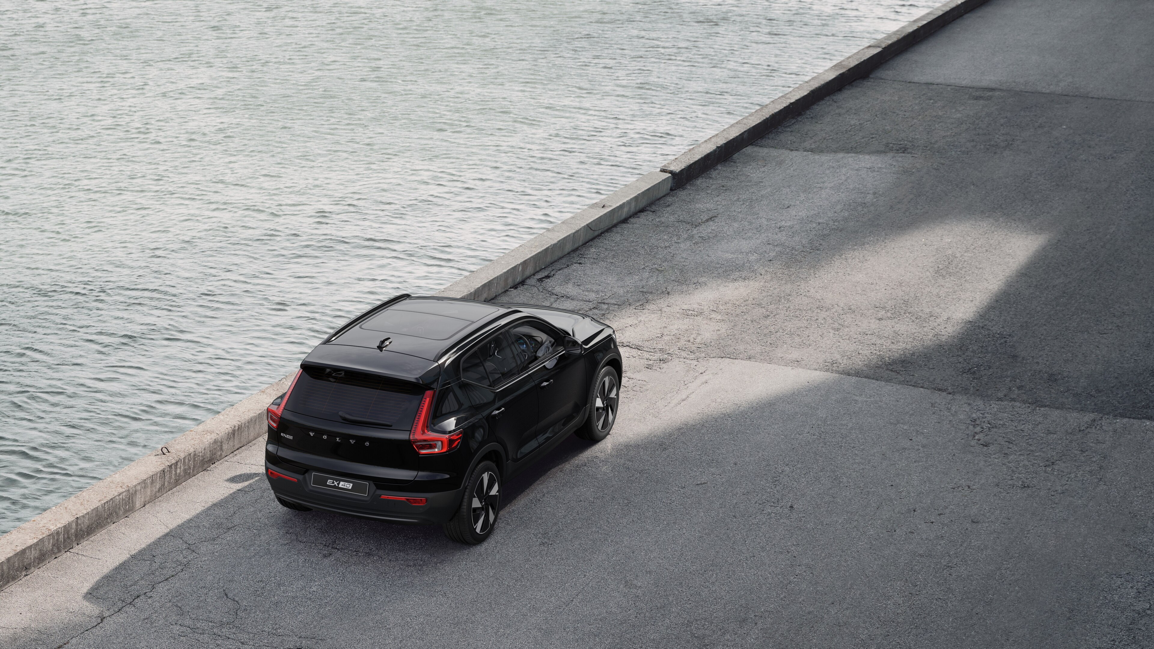 Volvo car rear view parked on quiet street beside water, with a paved walkway and water as the background.