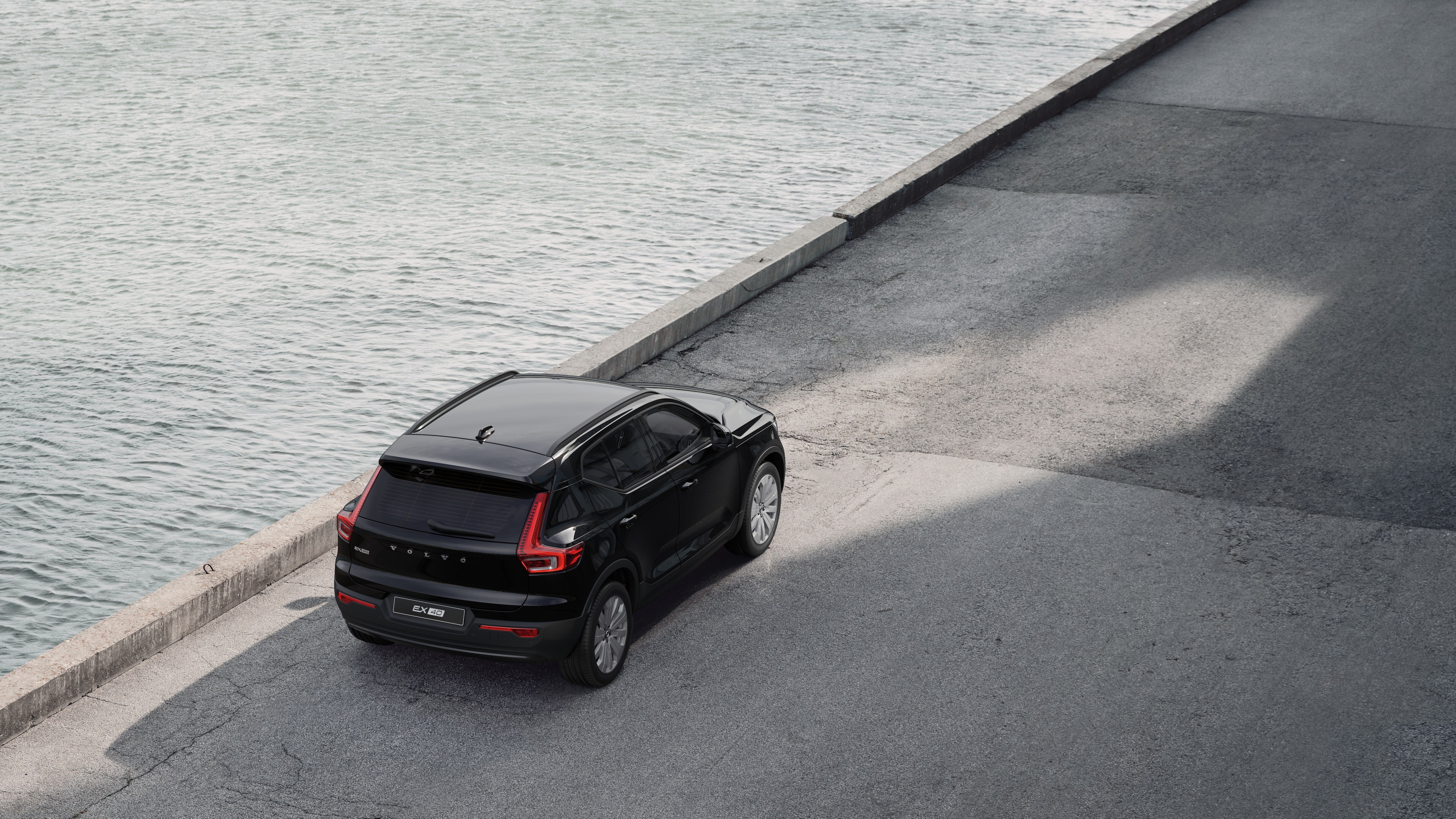Vista traseira do automóvel Volvo estacionado numa rua tranquila junto à água, com um passadiço pavimentado e água como pano de fundo.