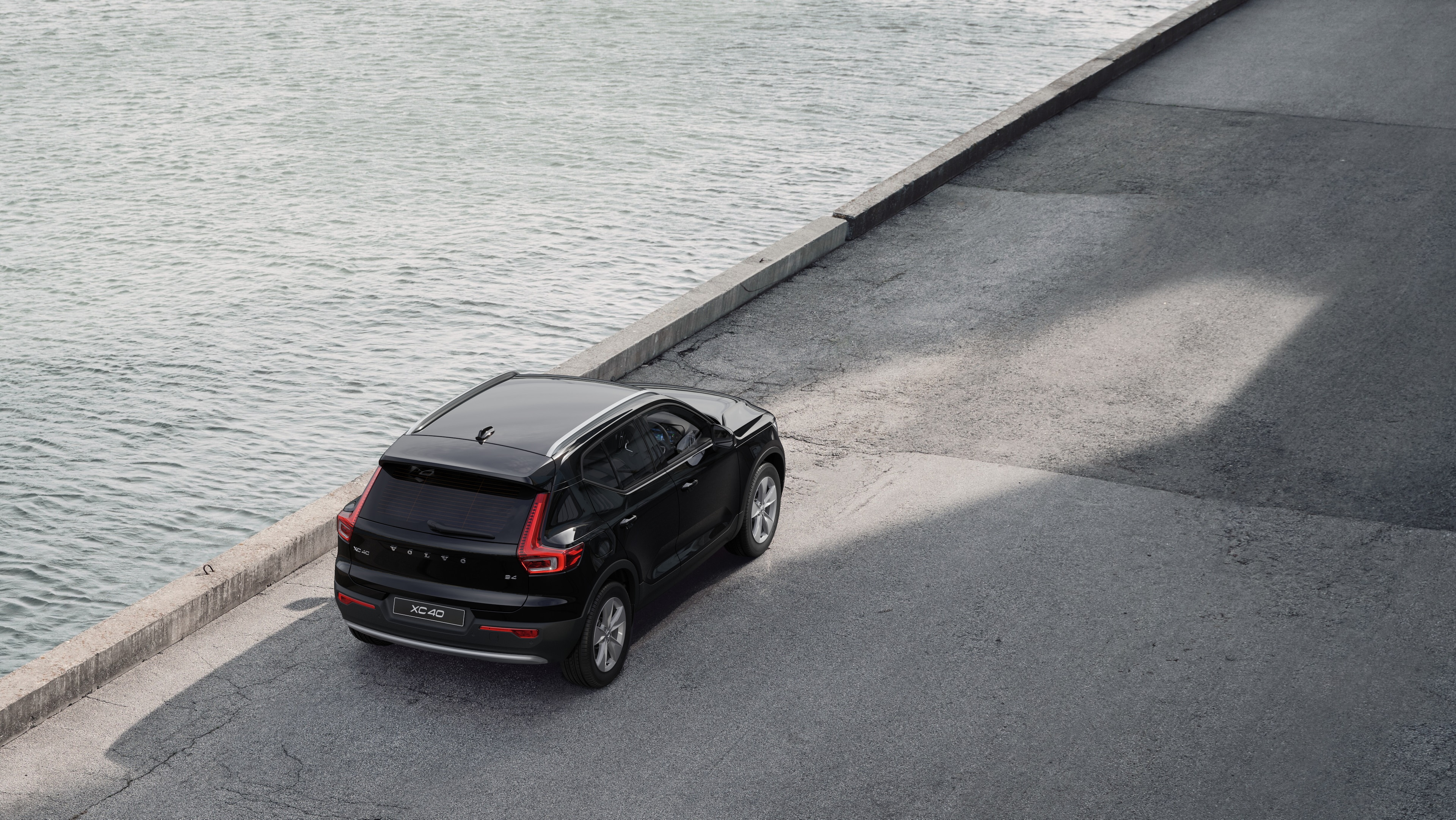 Volvo car rear view parked on quiet street beside water, with a paved walkway and water as the background.