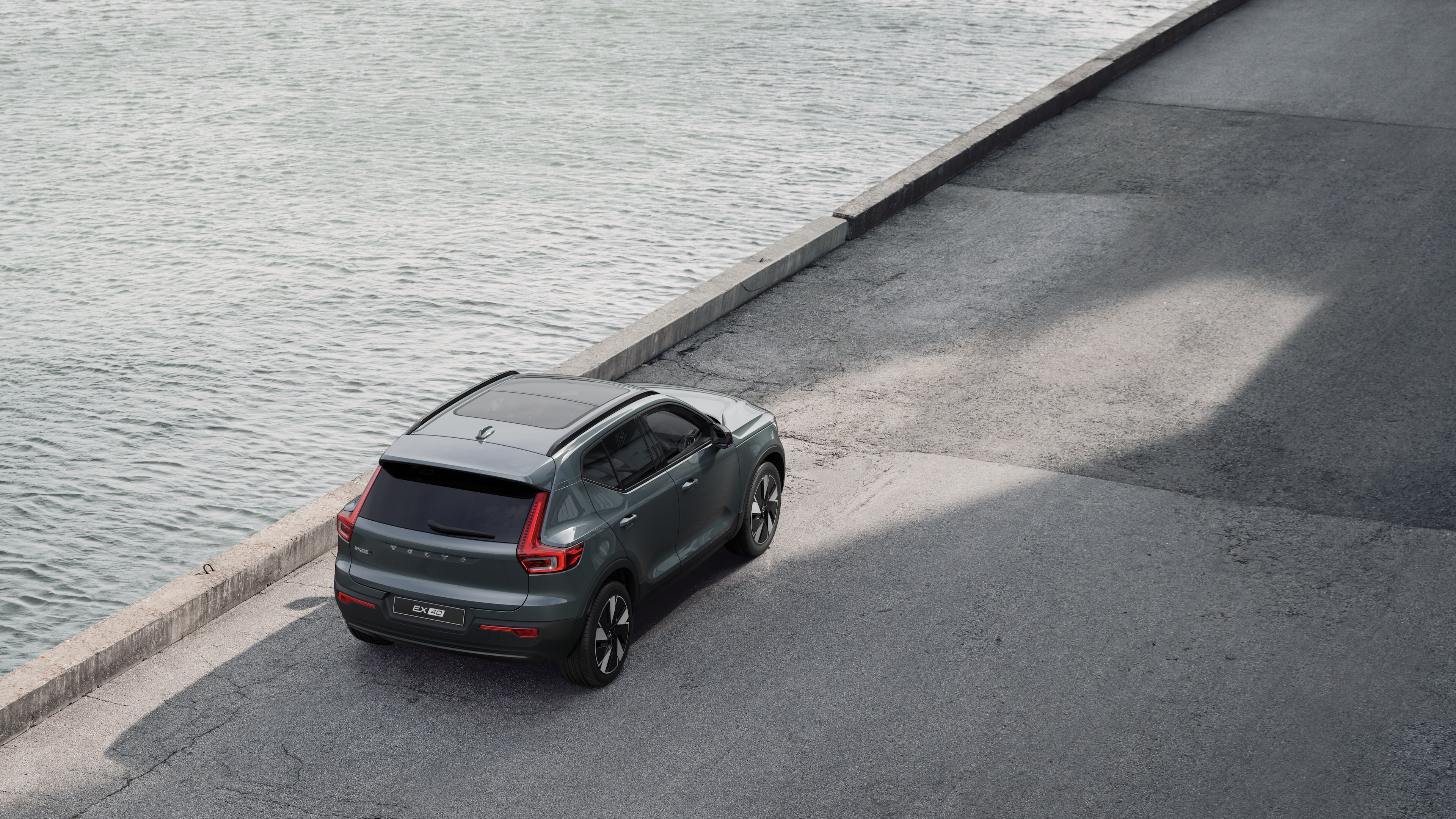 Volvo car rear view parked on quiet street beside water, with a paved walkway and water as the background.