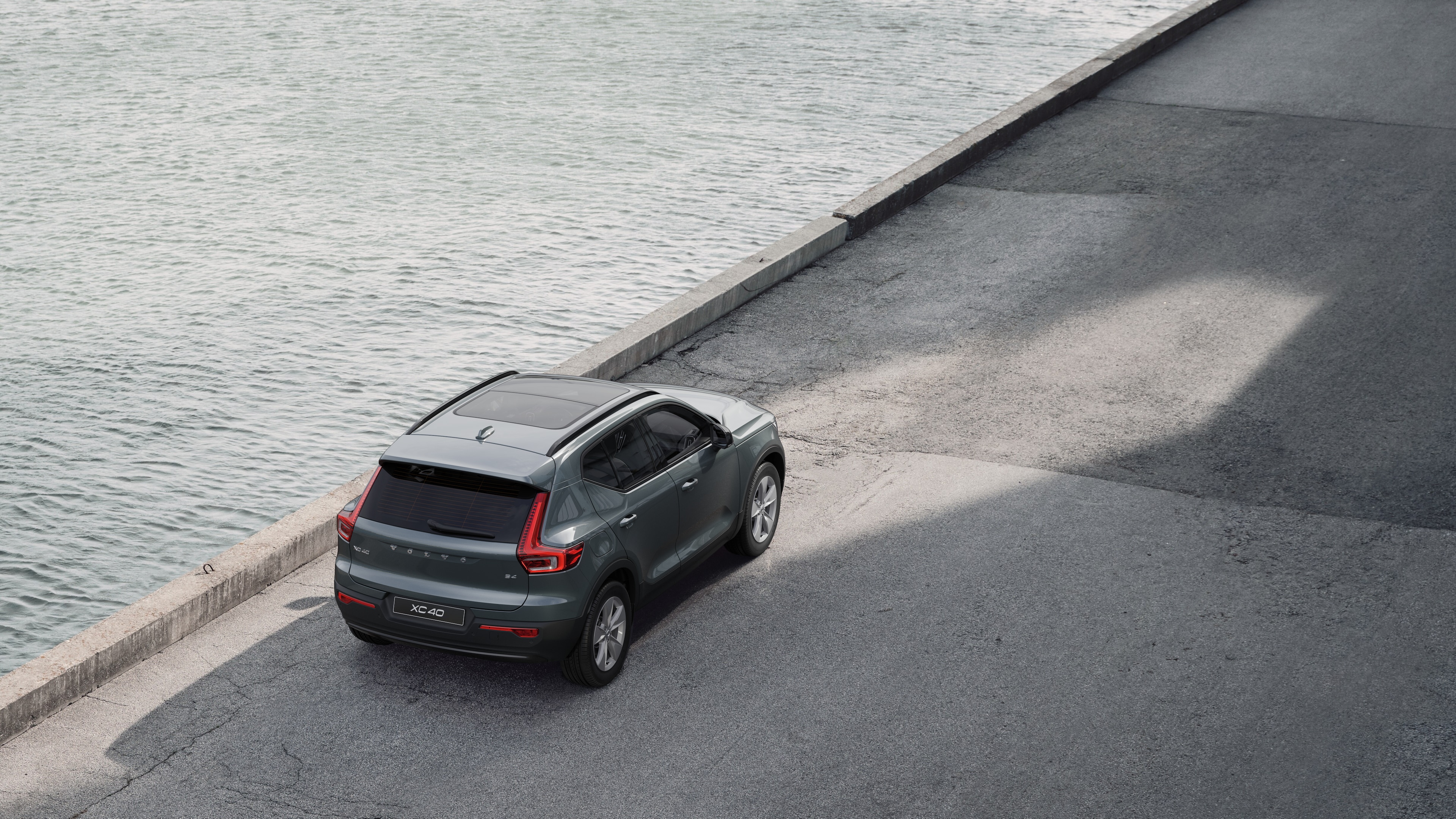 Volvo car rear view parked on quiet street beside water, with a paved walkway and water as the background.