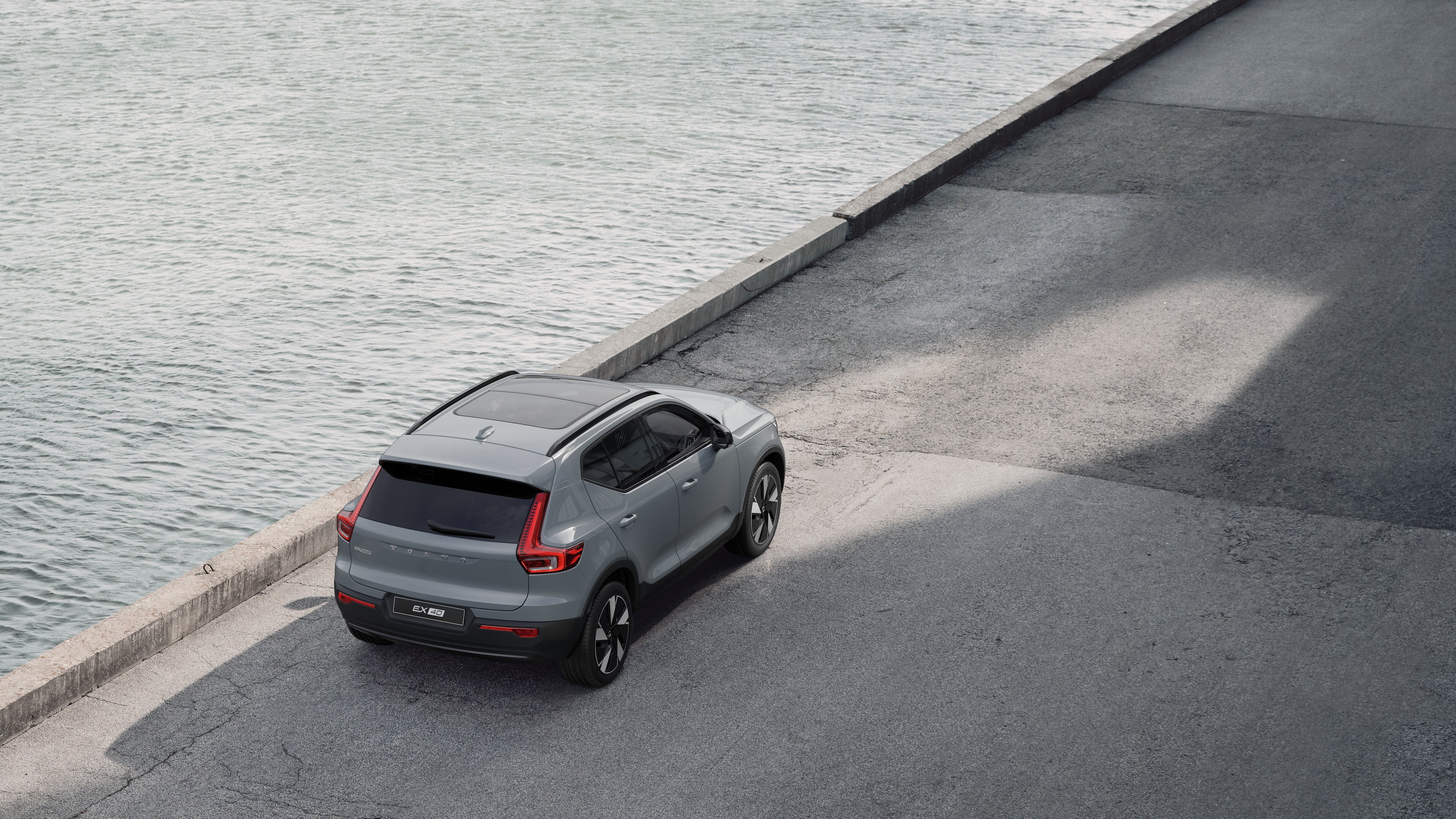 Volvo car rear view parked on quiet street beside water, with a paved walkway and water as the background.