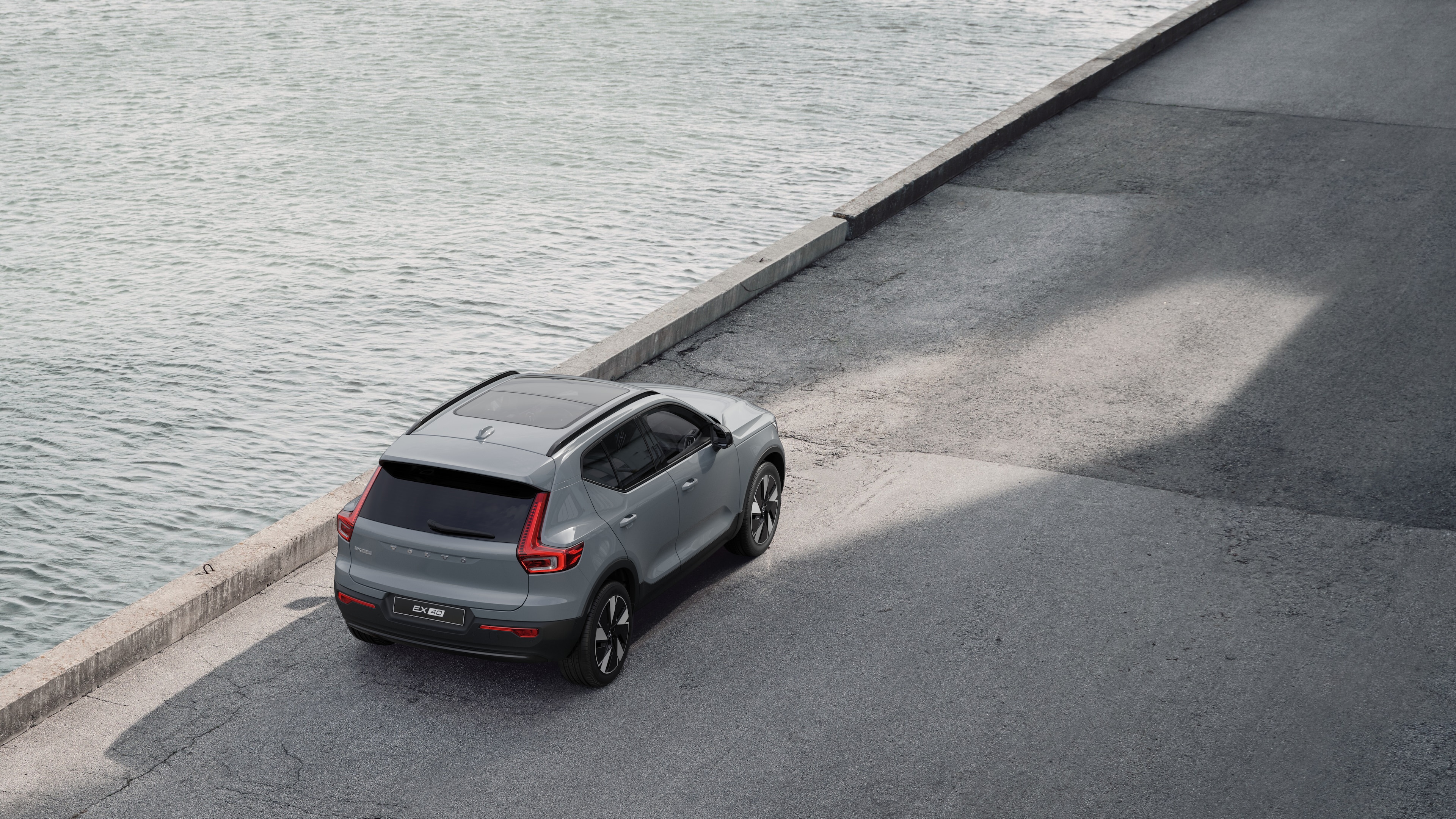 Volvo car rear view parked on quiet street beside water, with a paved walkway and water as the background.