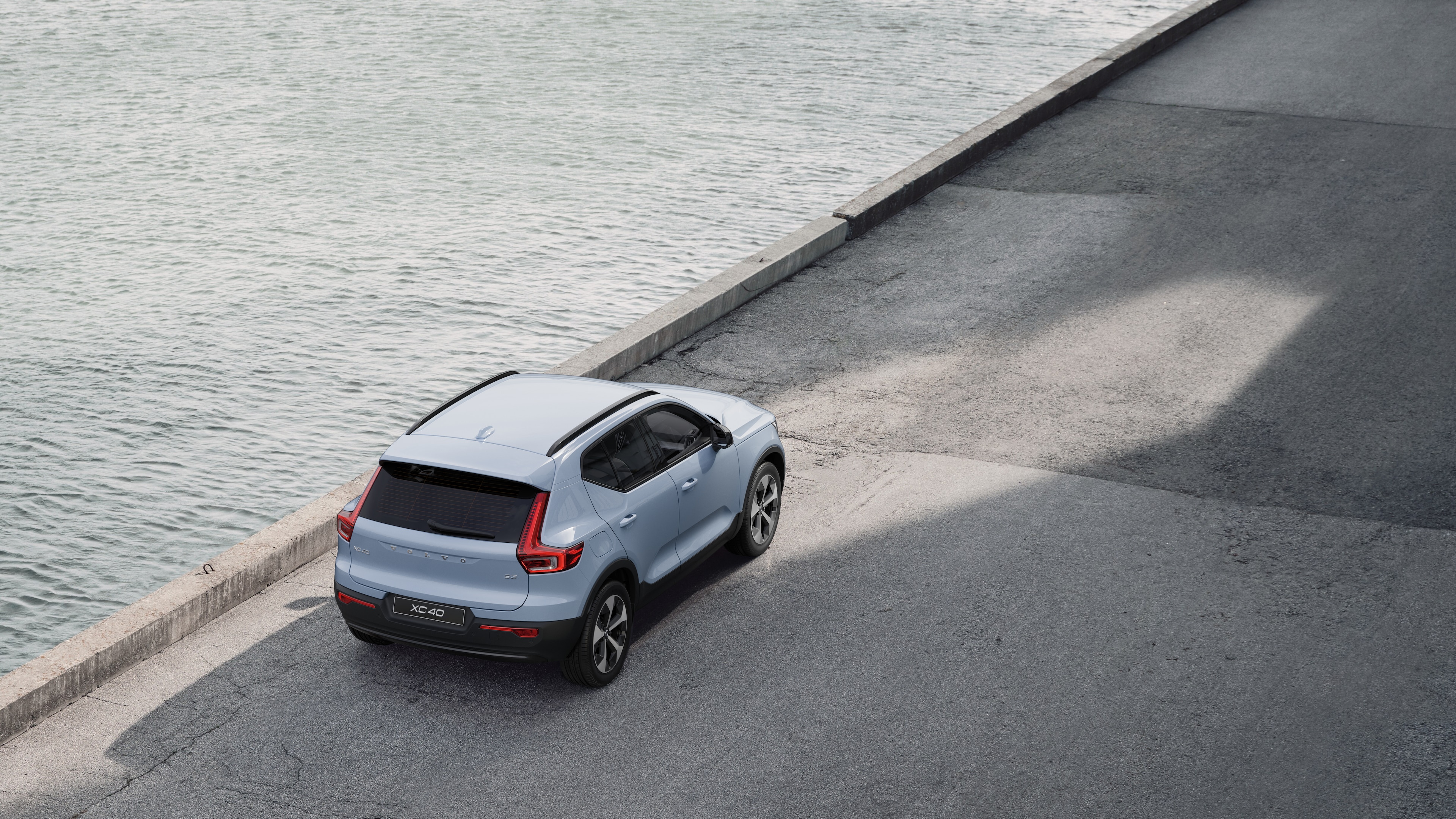Vue arrière d’une Volvo garée dans une rue calme au bord de l’eau, avec une allée pavée et de l’eau en arrière-plan.