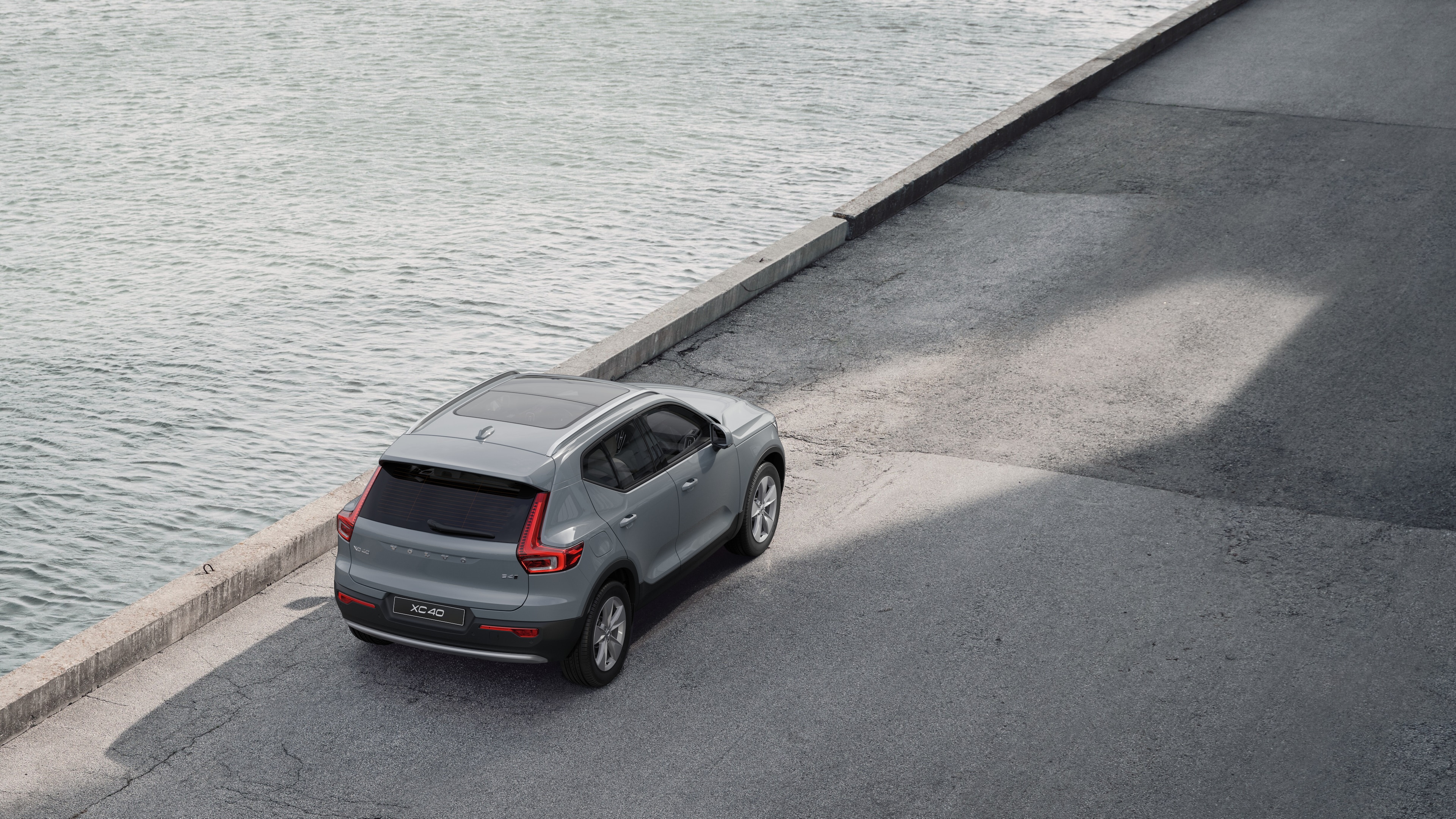 물가의 조용한 거리에 주차된 볼보 자동차 후면도, 포장된 보도와 물을 배경으로 합니다.