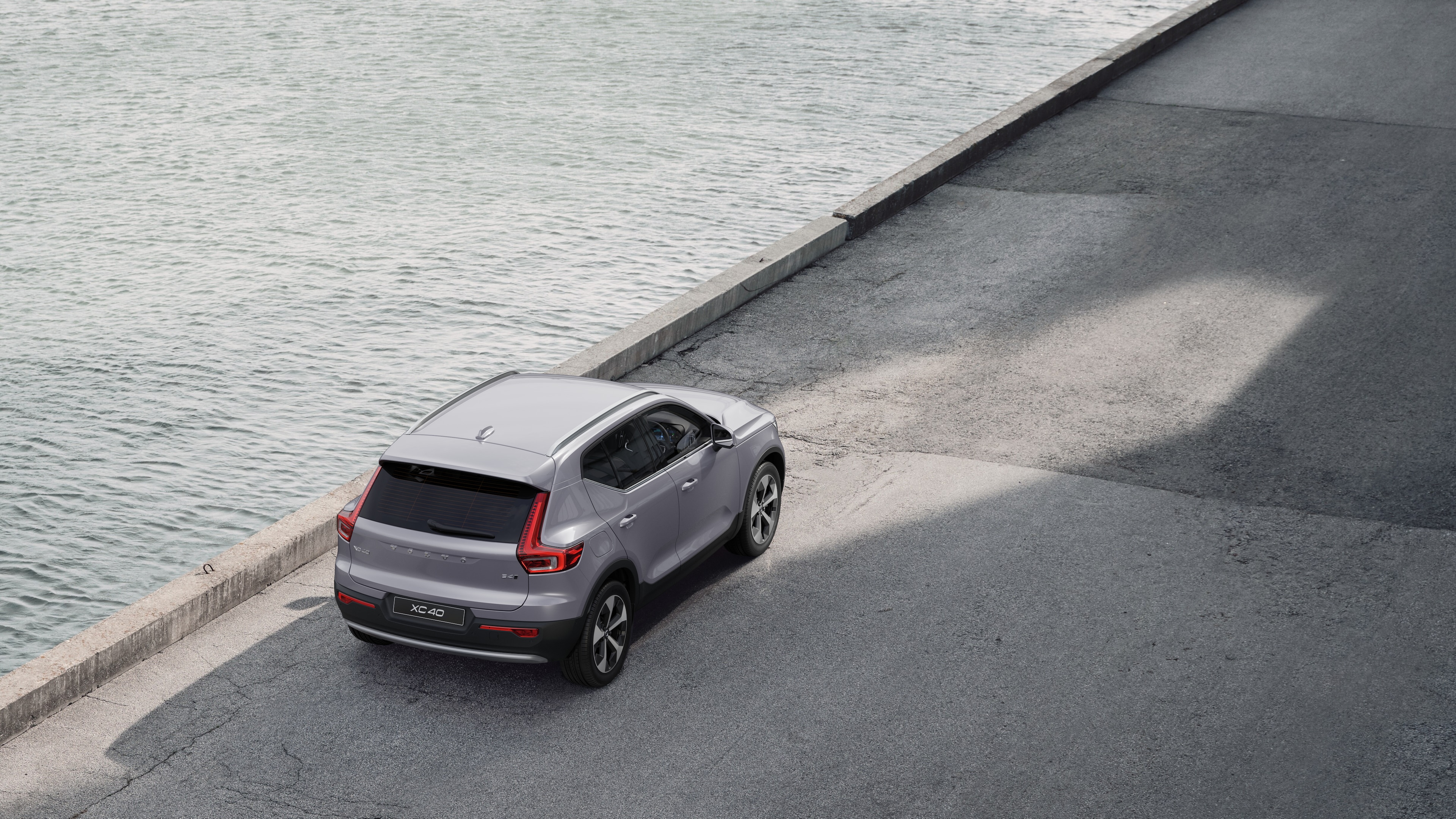 Volvo car rear view parked on quiet street beside water, with a paved walkway and water as the background.